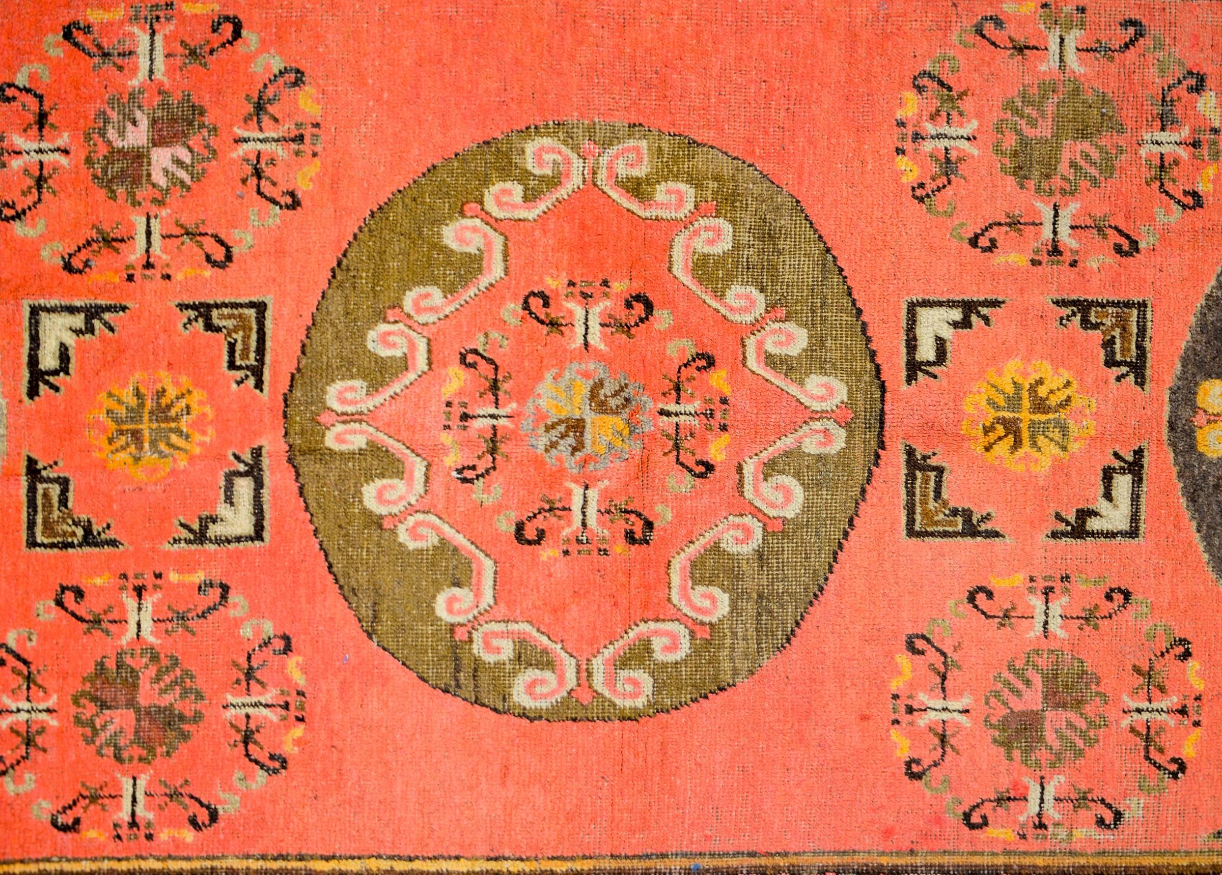 A wonderful early 20th century Central Asian Khotan rug with a three large round medallions amidst a field of smaller floral medallions, on a coral colored background. The border is composed of two patterned stripes. The inner stripe is a geometric