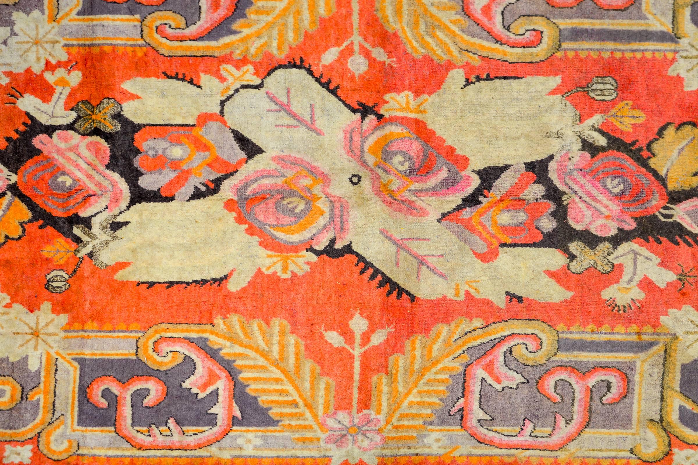An extraordinary early 20th century Central Asian Khotan rug with an incredible asymmetrical large-scale floral medallion woven in crimson, violet, pink, orange, black, and cream colored wool. The medallion lives amidst a crimson field with