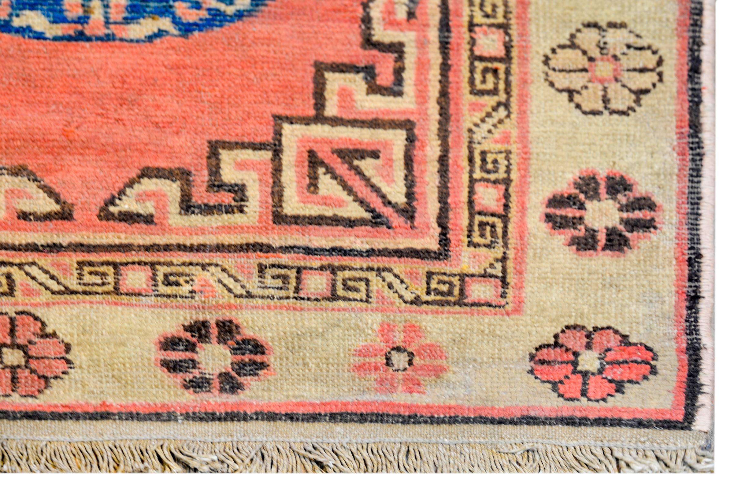 A beautiful early 20th century Central Asian Khotan rug with a three large round medallions amidst a field of swirling clouds, on a coral colored background. The border is composed of two patterned stripes. The inner stripe is a geometric pattern