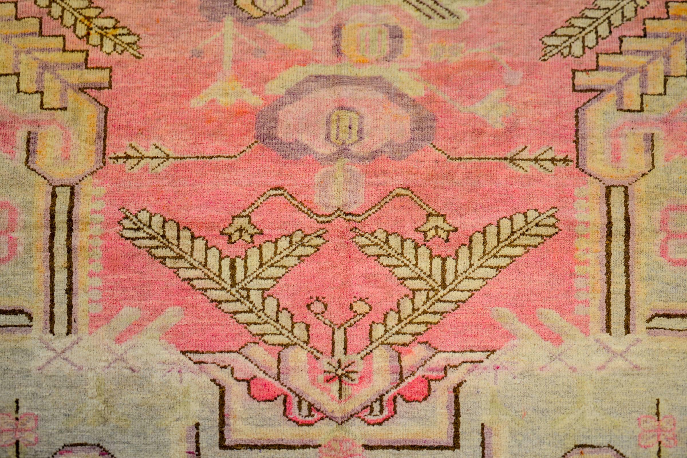 A wonderful early 20th century Central Asian Khotan rug with an incredible asymmetrical large-scale floral medallion woven in crimson, violet, black, and cream colored wool. The medallion lives amidst a pink field with flowering branches surrounded
