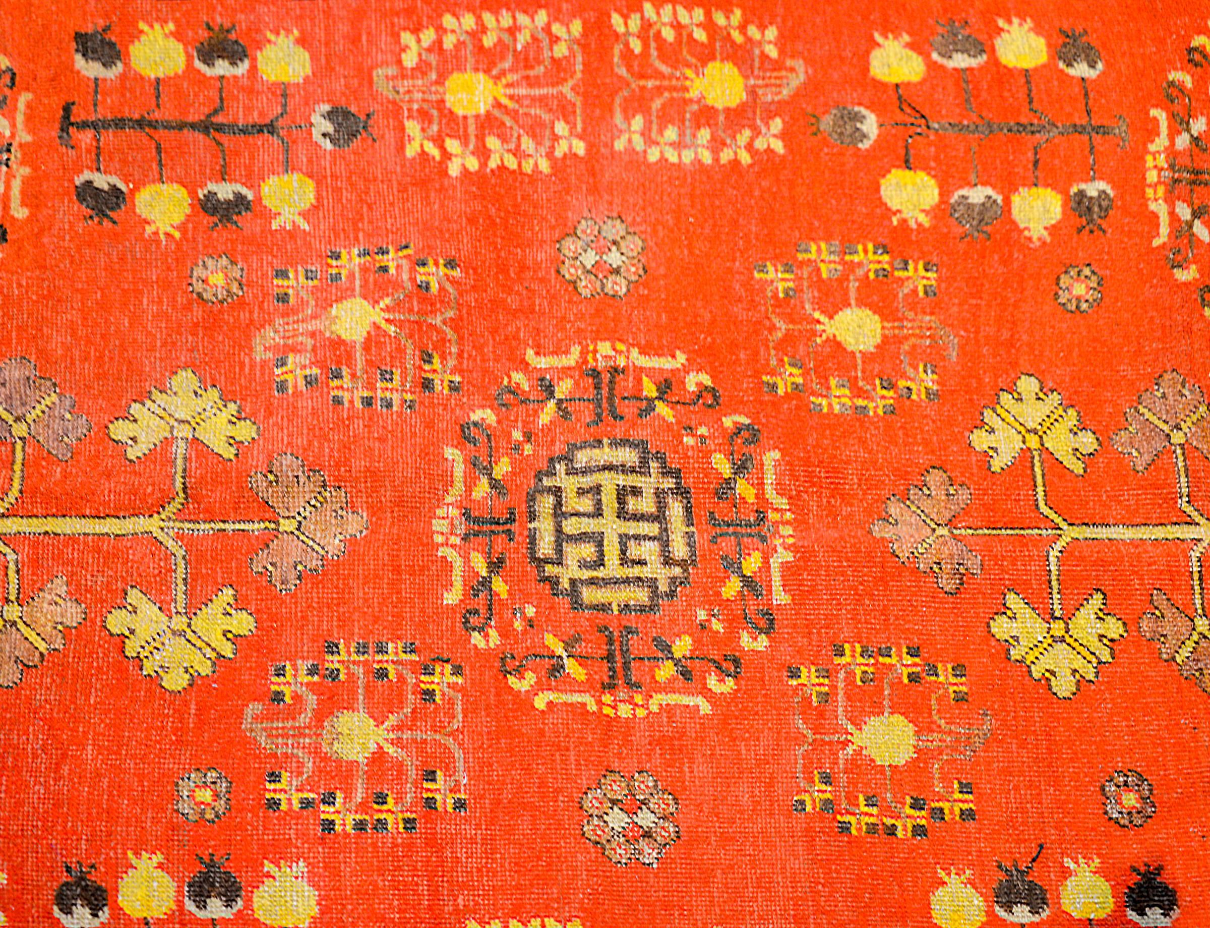 A beautiful early 20th century Central Asian Khotan rug with a rich crimson field of pomegranate, trees-of-life, and floral patterns. The border is wonderfully rendered consisting of a Buddhist meandering motif pattern and a turbulent cloud motif,