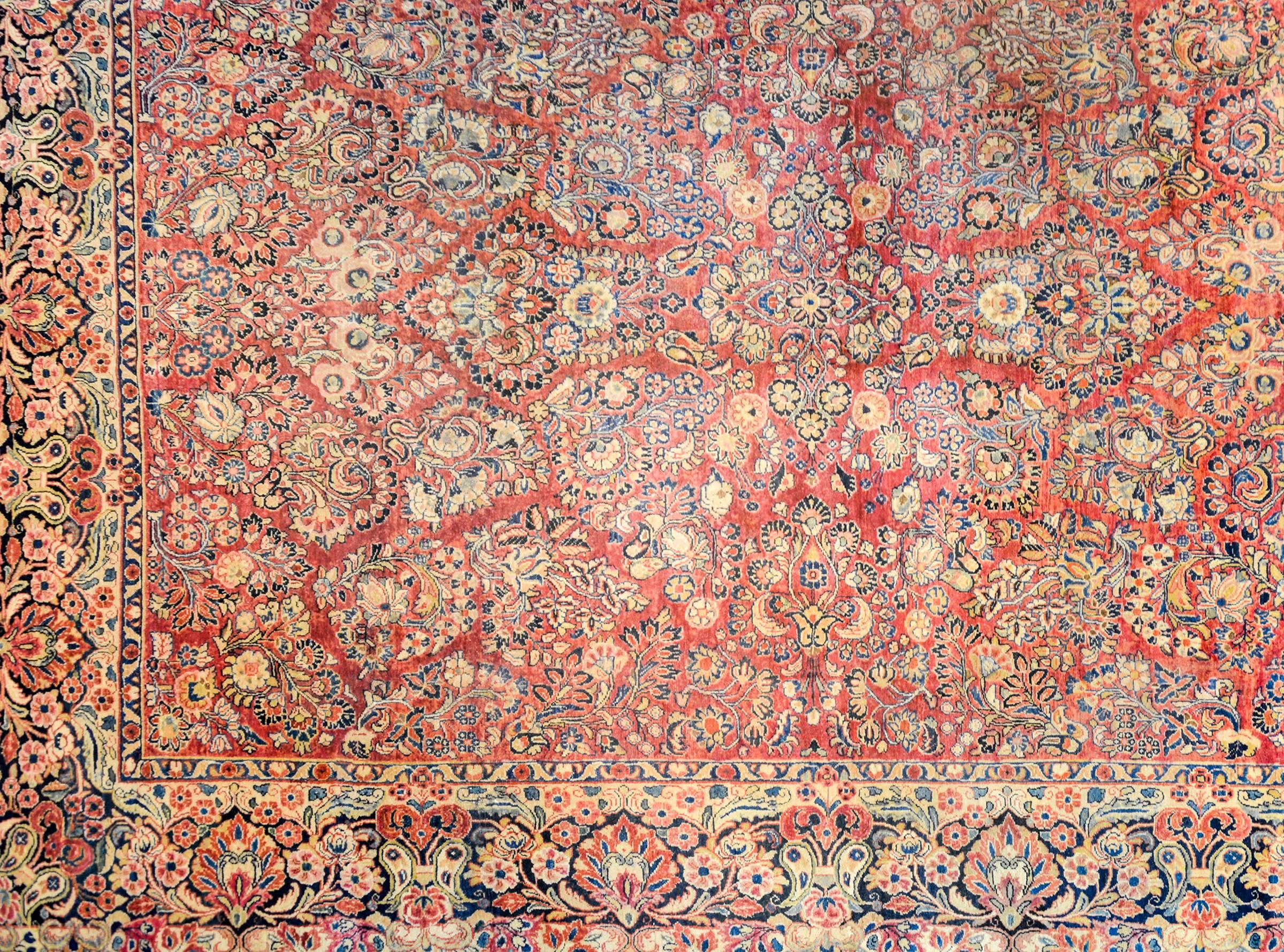 An exceptional early 20th century Persian Sarouk rug with a beautiful mirrored floral and vine pattern woven in light and dark indigo, pink, brown, green and gold, on a rich cranberry background. The border is wonderfully rendered with a large-scale
