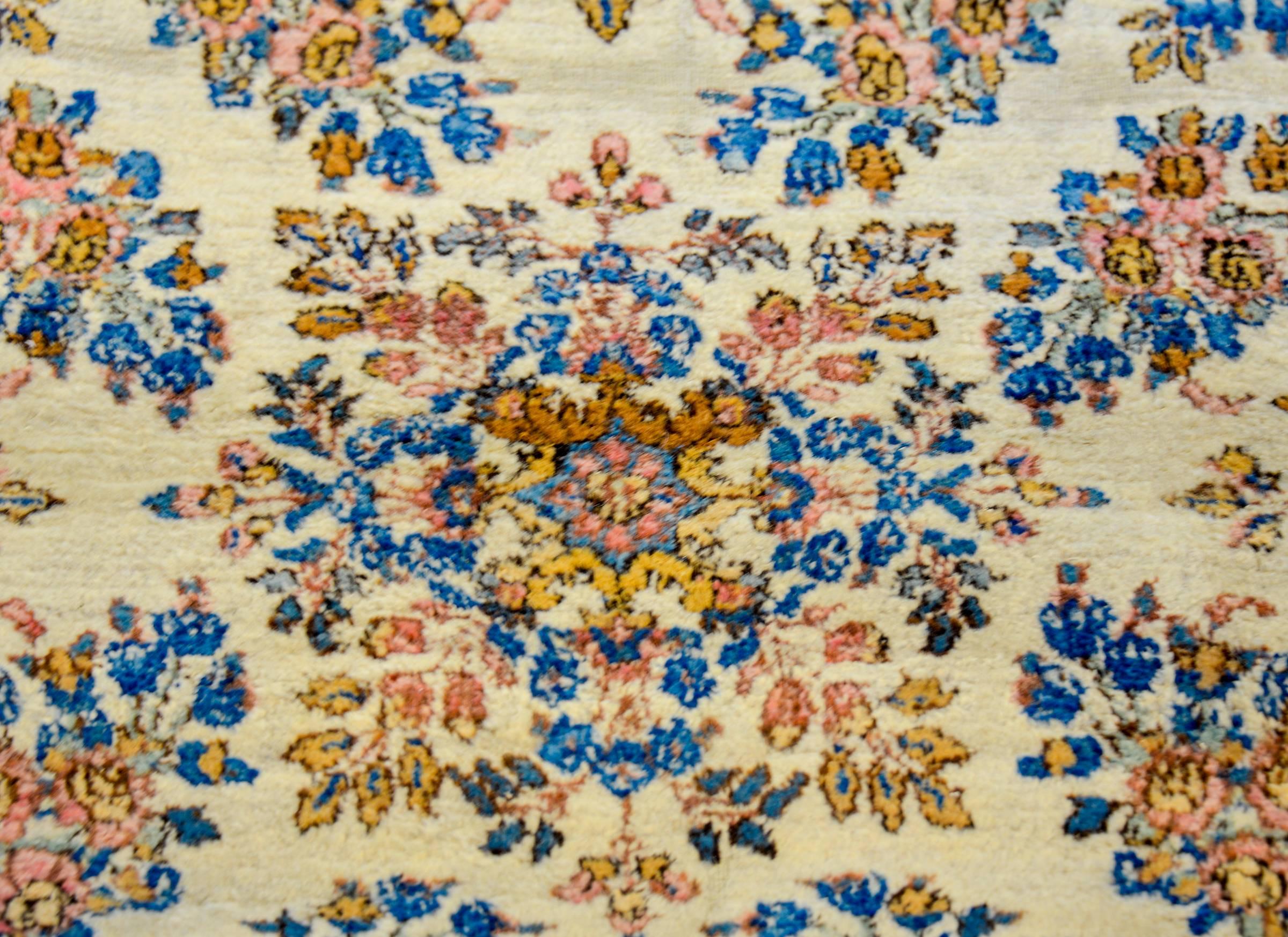 Un étonnant tapis Kirman presque carré, datant du début du 20ème siècle, tissé avec une laine végétale de qualité supérieure, brillante et soyeuse, de couleur indigo et or, avec un grand médaillon floral en forme de diamant. La bordure est