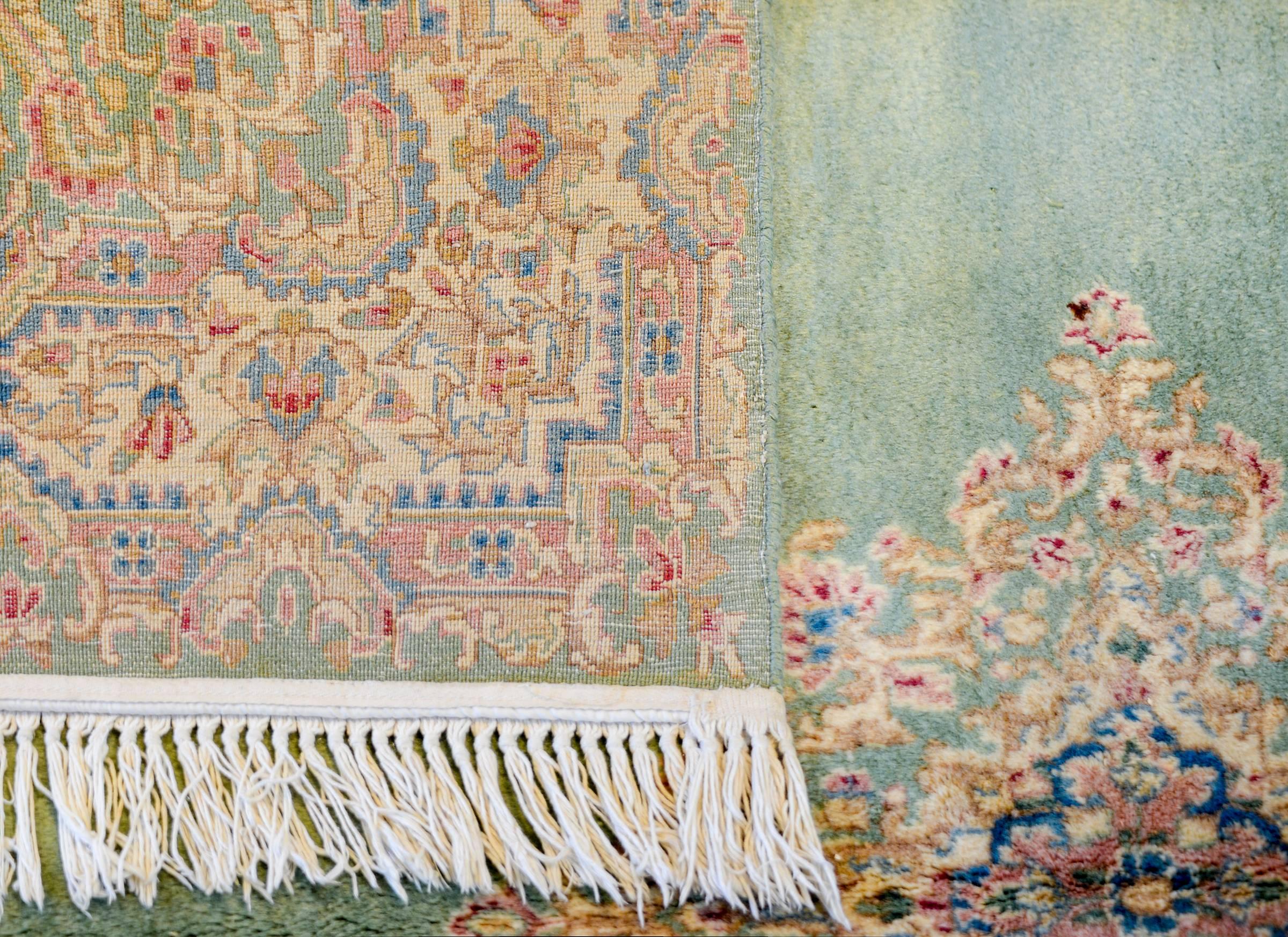 An amazing early 20th century Persian square Kirman rug woven with an incredibly high quality shimmering silky vegetable dyed wool with a large floral diamond medallion living on a sage green background surrounded by a fantastic baroque floral