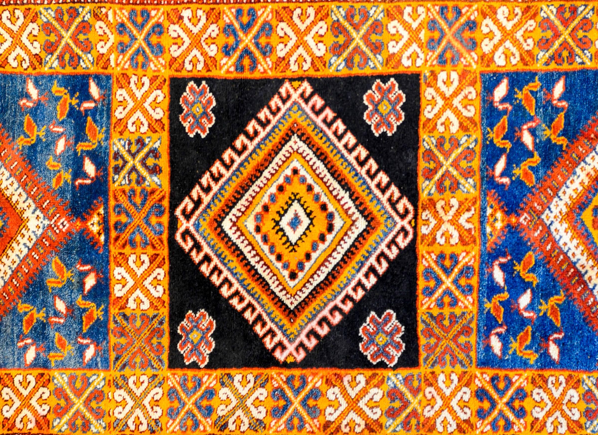 A bold vintage Moroccan runner with a diamond medallion on a black background flanked by two matching medallions woven with a fantastic palate of brilliant crimson, indigo, orange, and gold vegetable dyed wool, amidst a field of red and white birds.