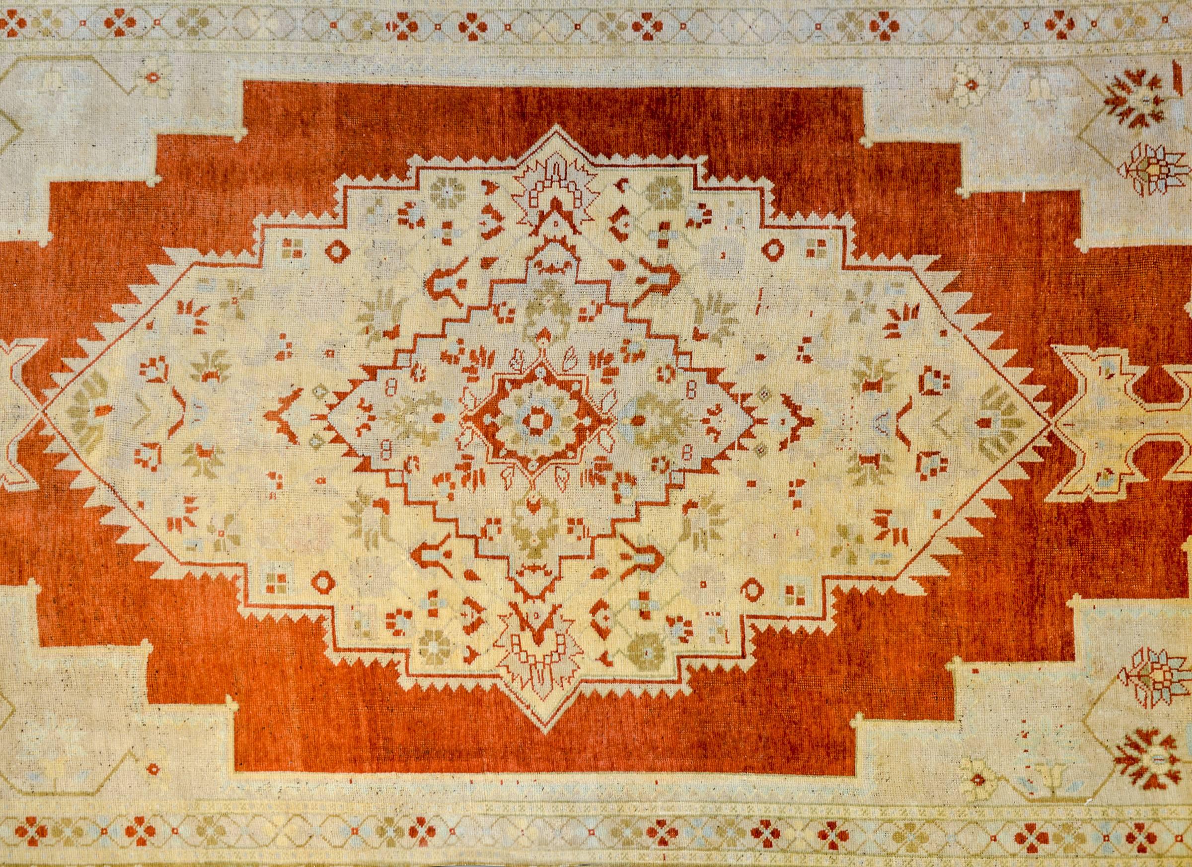 A vintage Turkish Oushak rug with a beautiful pattern woven in orange, gold, green, and cream colored wool. The border is exceptional, with large-scale wide stylized floral and leaf patterned stripe flanked by a matching petite floral and vine
