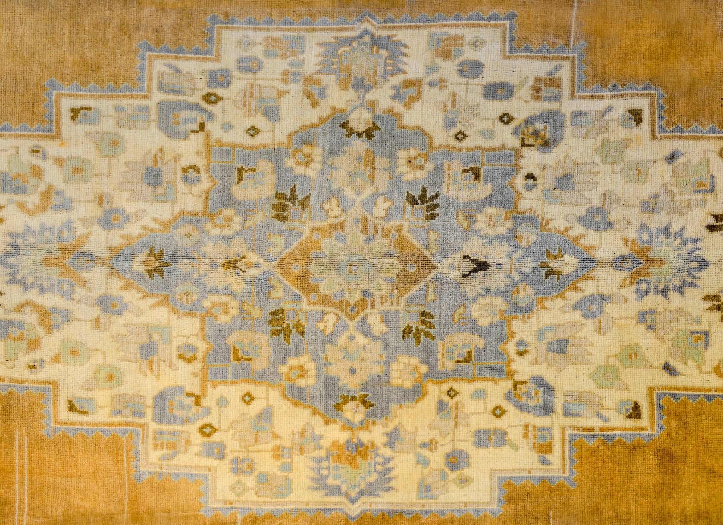 A vintage Turkish Oushak rug with a beautiful diamond medallion amidst a field of flowers woven in gold, indigo, brown, and cream color wool. The border is exceptional, with large-scale wide stylized floral and leaf pattern flanked by different