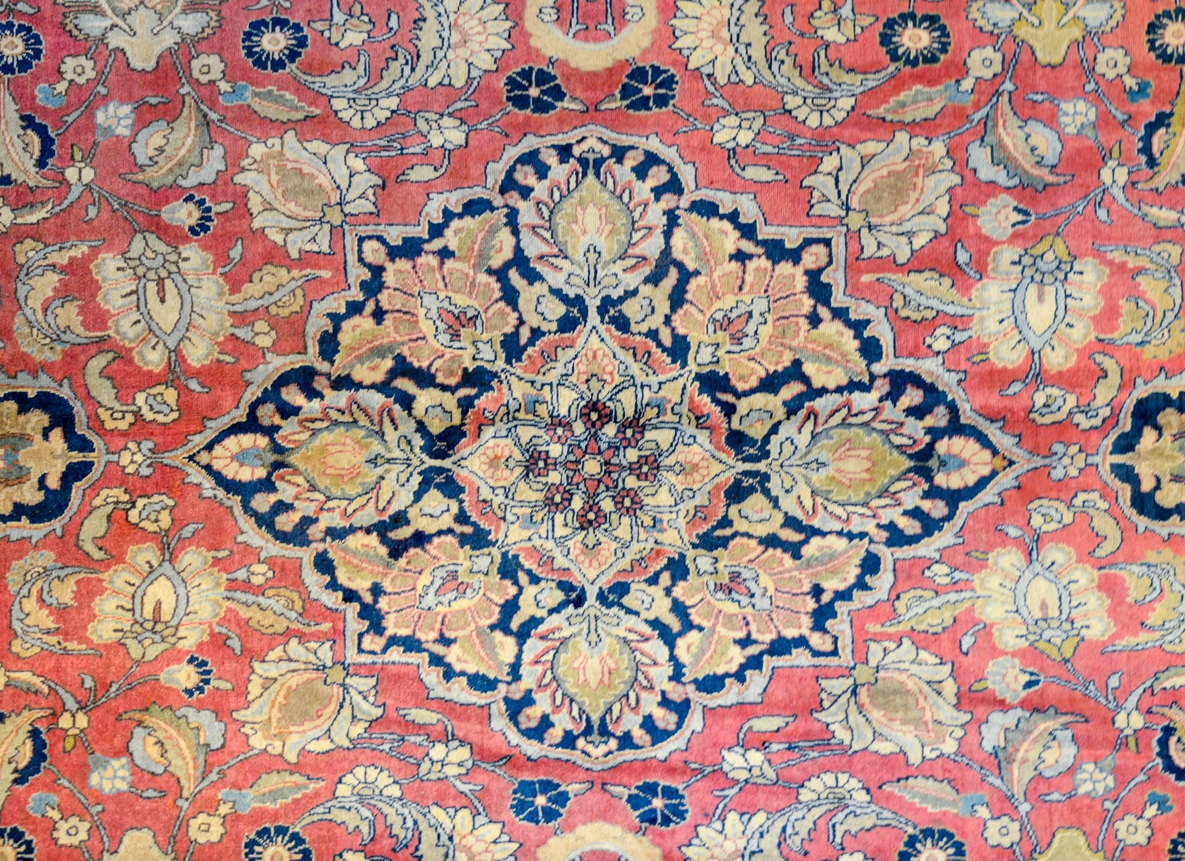 An incredible mid-20th century Persian Tabriz rug with a fantastic pattern of intricately and tightly woven pattern containing a large central medallion amidst a field of flowers and scrolling vines all woven in gold, pink, green, and light and dark