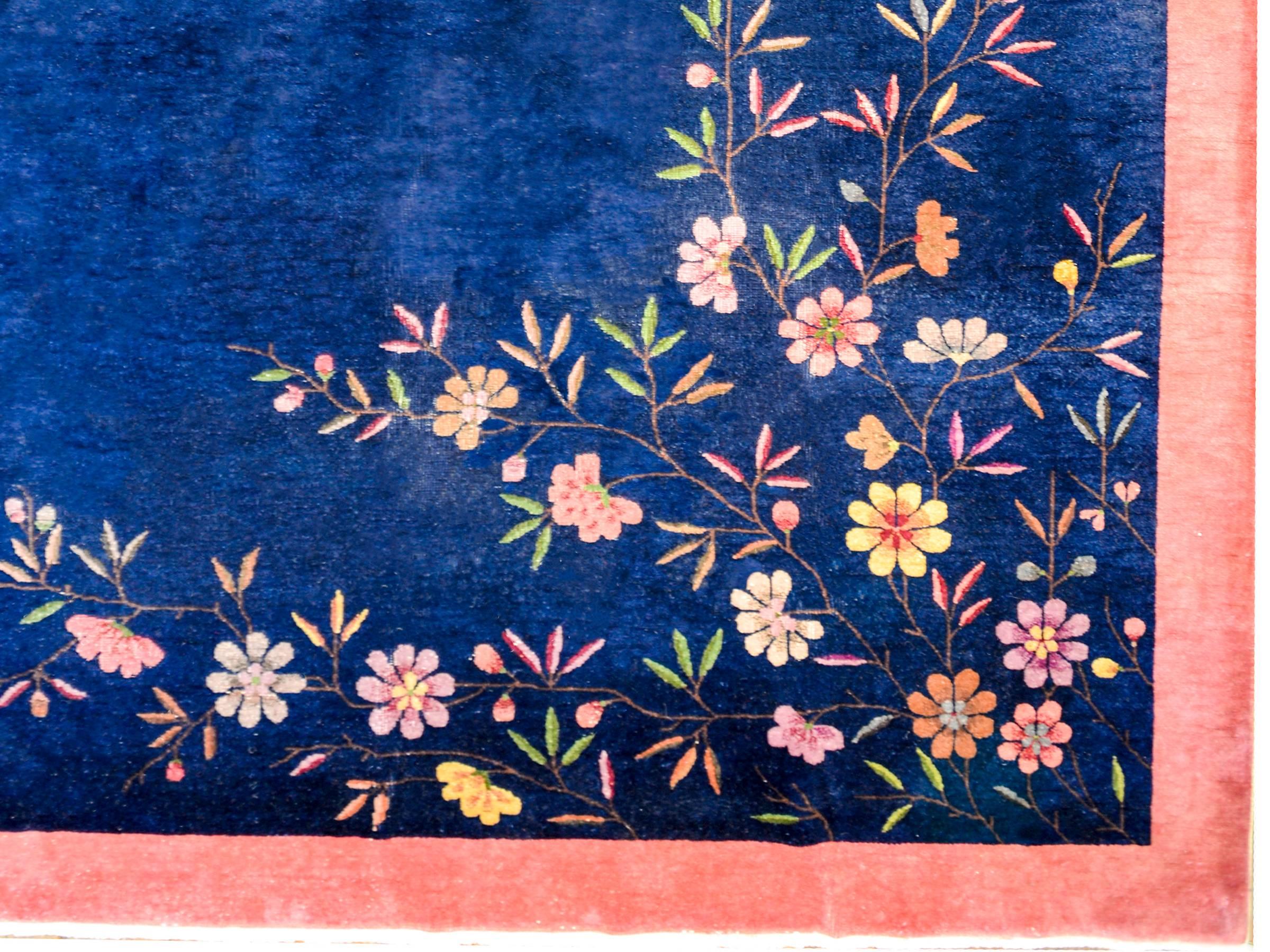 A beautiful Chinese Art Deco rug with a wonderful rich indigo field surrounded by a soft salmon border. One corner contains multicolored chrysanthemums and the other contains multicolored peonies.