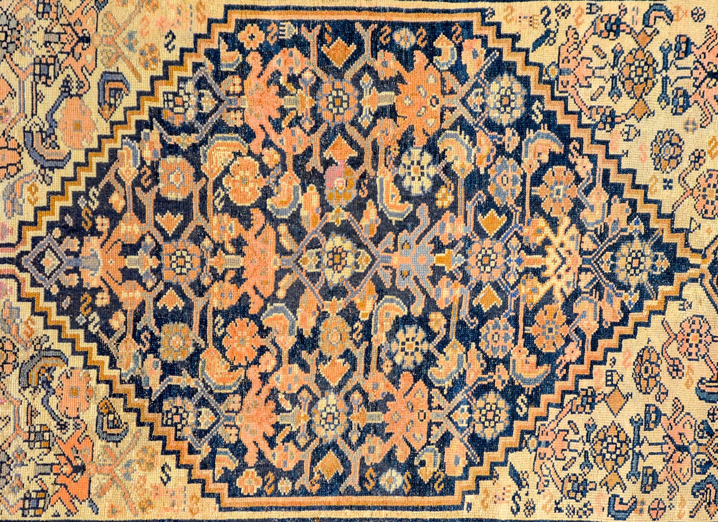 A wonderful early 20th century Persian Azari rug with a large diamond medallion with a light indigo, gold, and orange lattice floral and vine pattern on a dark indigo background amidst a field of similarly designed floral lattice patterned field.
