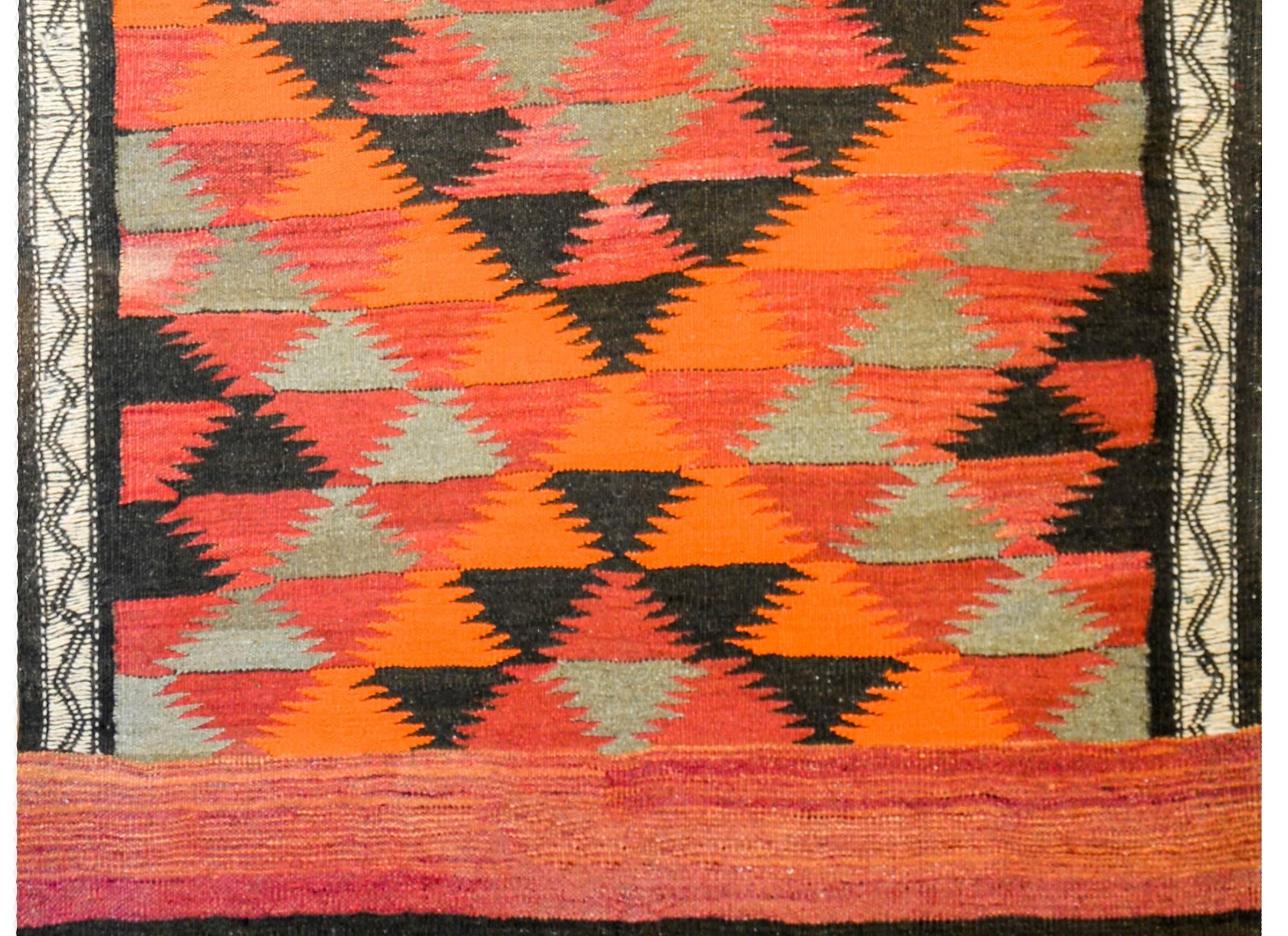 A fantastic vintage Afghani Kilim rug with a bold all-over diamond pattern with crimson, orange, black, and green diamonds. The ends are composed of three wide colored stripes, with a fringe end.