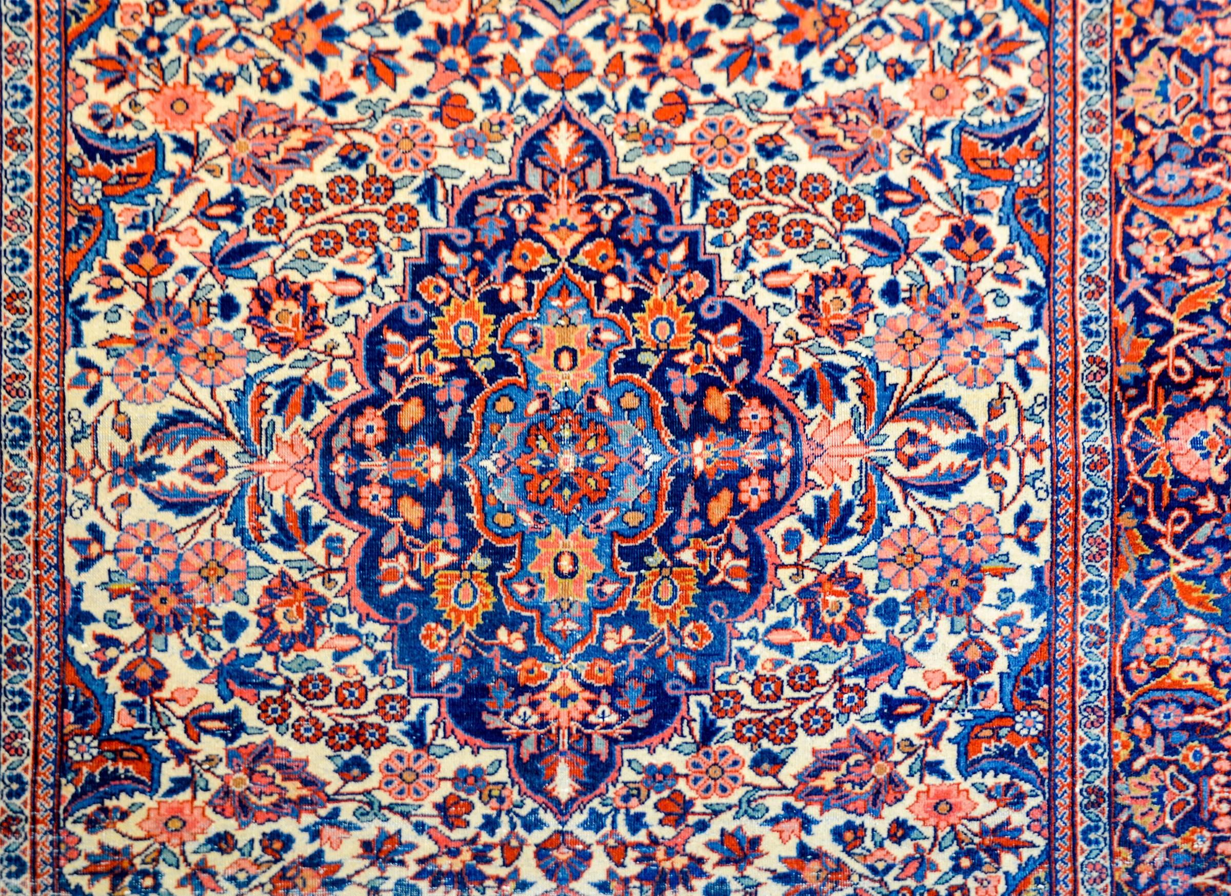 An exceptional early 20th century Persian Kashan rug with a densely woven field and medallion of myriad flowers, leaves, and vines, all woven in crimson, indigo, gold, pink, and cream colored vegetable dyed wool. The border is as densely woven as
