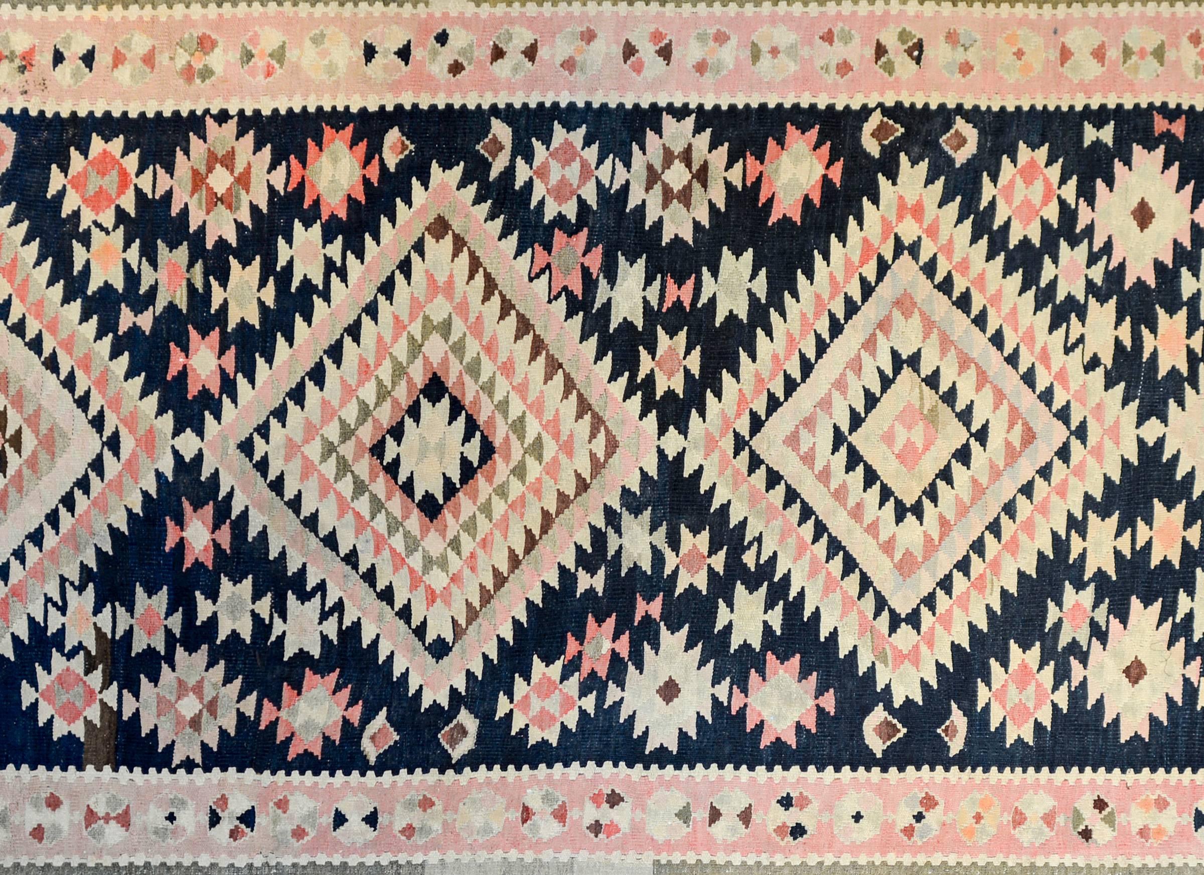 A wonderful early 20th century Persian Zarand Kilim runner with four large-scale diamond medallions amidst a field of stylized flowers on an indigo background.  The border is contrasting, with a wide central stripe with stylized flowers flanked by