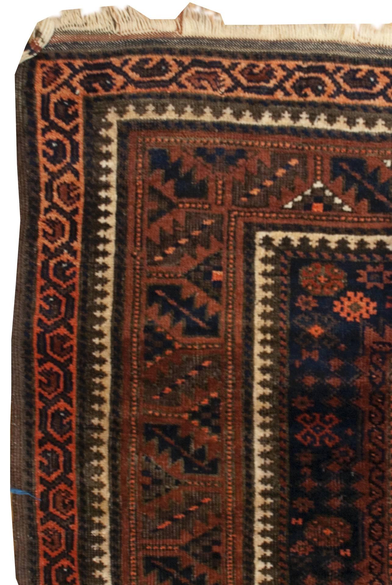 An early 20th century Persian Baluch rug with eight rectangular medallions on an indigo background amidst a field of flowers, and surrounded by multiple complementary geometric and floral borders.