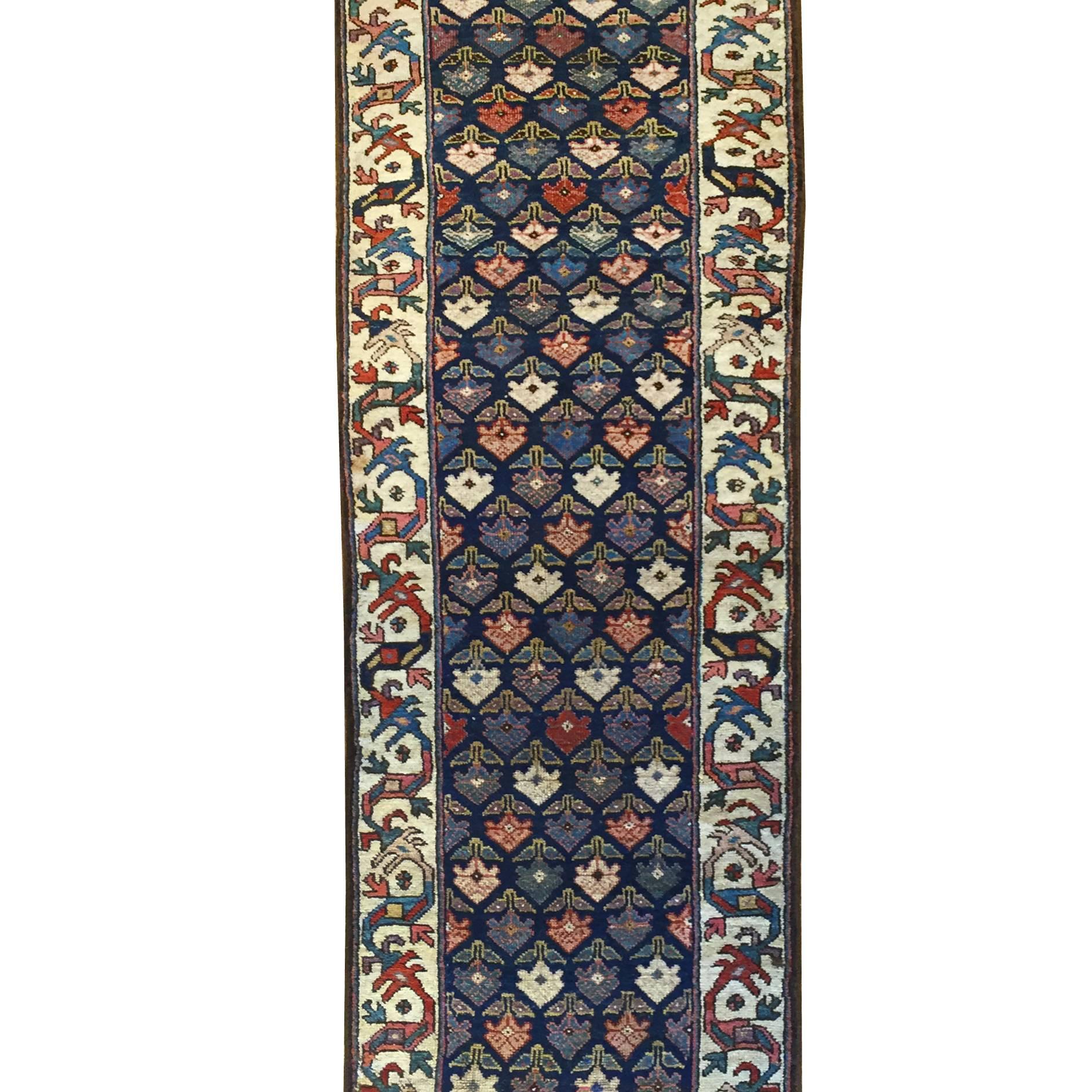 An amazing 19th century Azerbaijani Kuba runner, woven in 100% vegetable dyed wool, with an all-over multicolored pattern of flowers with two leaves on an indigo background with a wonderful large-scale scrolling vine and floral border on a wide