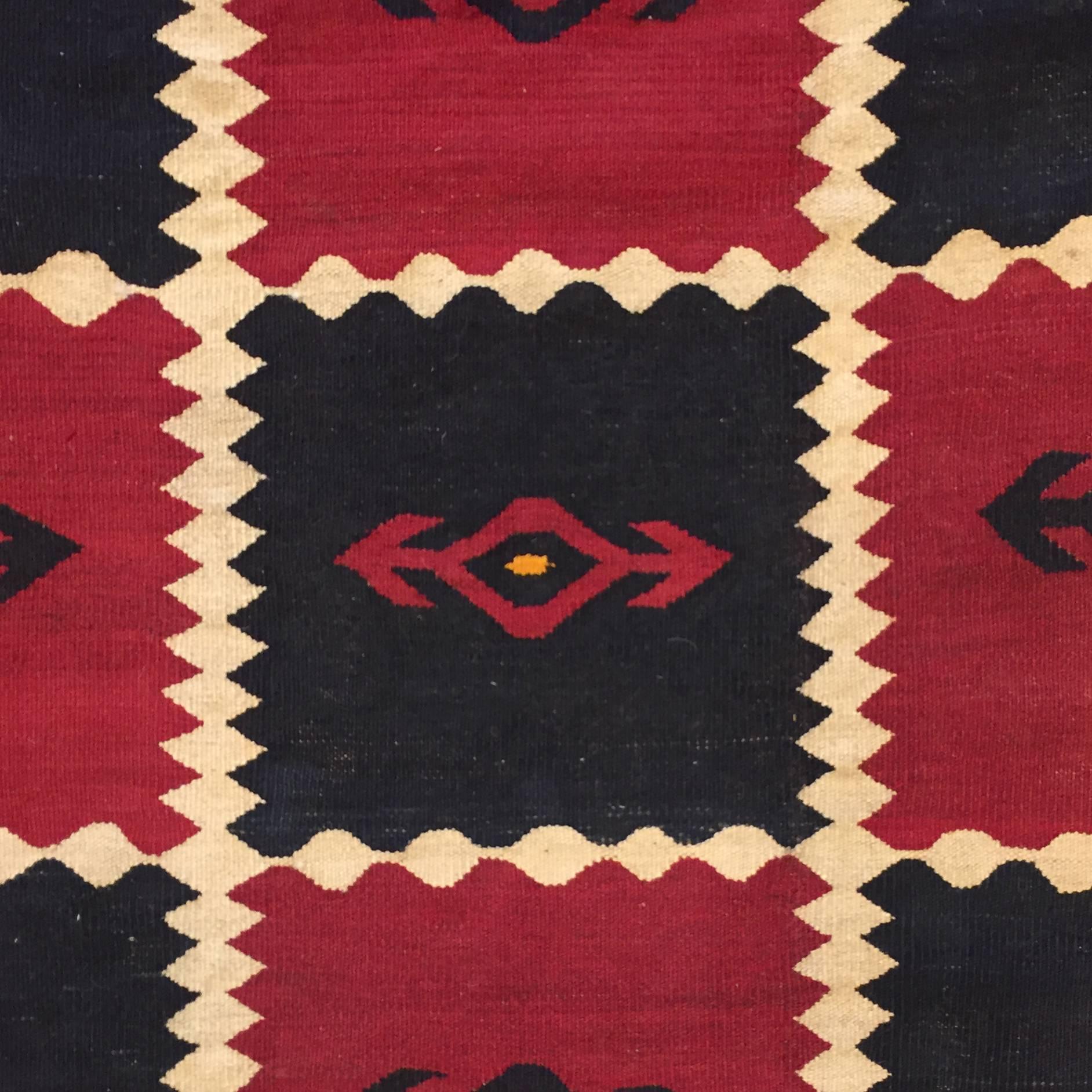 A mid-20th century Uzbek Kilim rug with a large-scale alternating crimson and black pattern, each with a double-arrowed motifs, divided with zig-zag stripes, and surrounded by a wide natural brown wool borders with matching double-arrowed motifs,