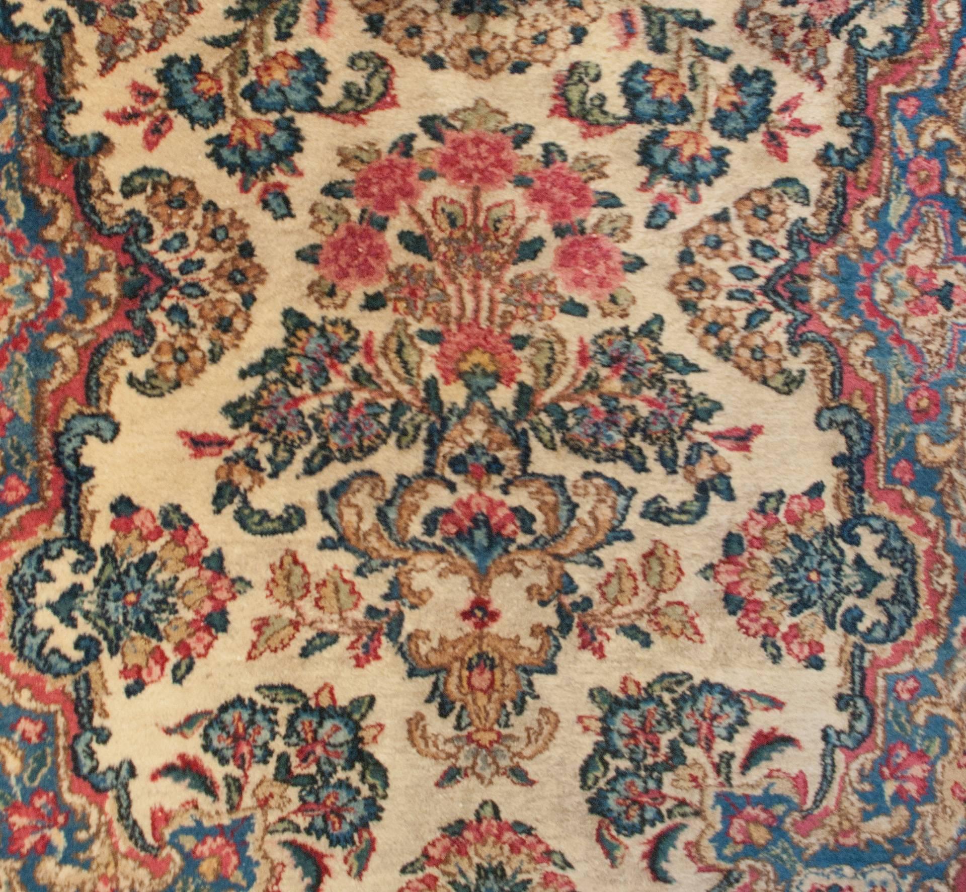 Un runner persiano Kirman dell'inizio del XX secolo con un motivo abilmente tessuto di fiori indaco, rossi, rosa e verdi su uno sfondo di lana naturale non tinta, circondato da un elaborato bordo di colori simili.