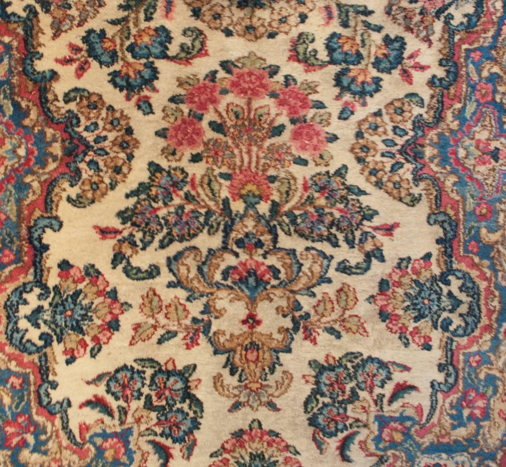 An early 20th century Persian Kirman runner with a skillfully woven pattern of indigo, red, pink, and green flowers on a natural, undyed, wool background, surrounded an elaborate border of similar colors.