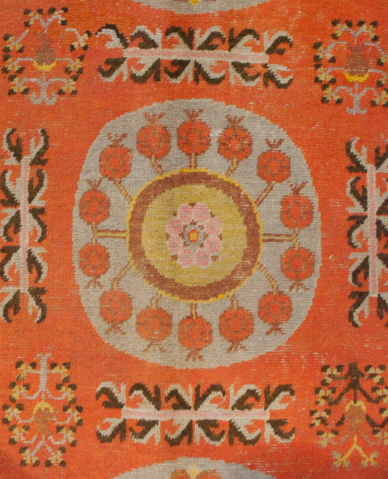 An early 20th century central Asian Khotan rug with three large circular light blue medallions with wonderful yellow, lime green, pink and orange floral patterns, on an orange background amidst a field of flowers. The rug is surrounded by three
