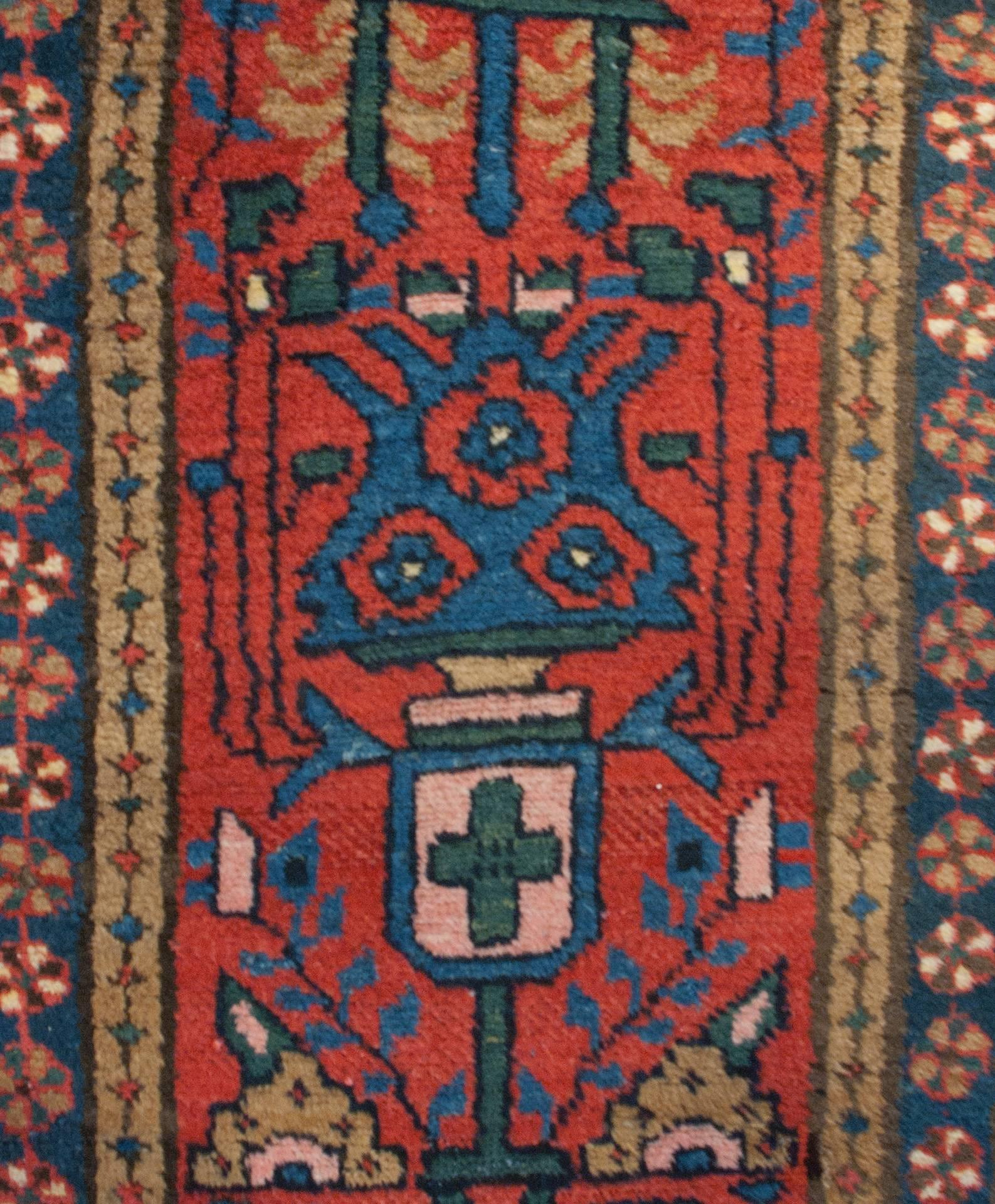 An early 20th century Persian Heriz runner with a bold indigo, emerald and taupe floral pattern on a crimson background, surrounded by a matching diamond motif border on either side of a round multicolored floral border on an indigo background.
