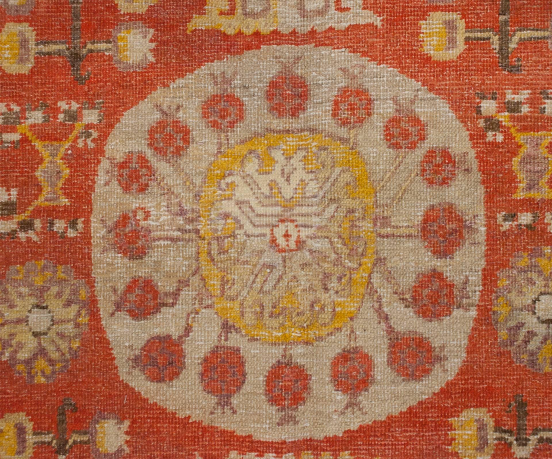 An early 20th century Central Asian Khotan rug with a wonderful large pale indigo central medallion with a pomegranate motif surrounding a gold floral center, on a rich crimson field of flowers and more pomegranates, surrounded by two distinct