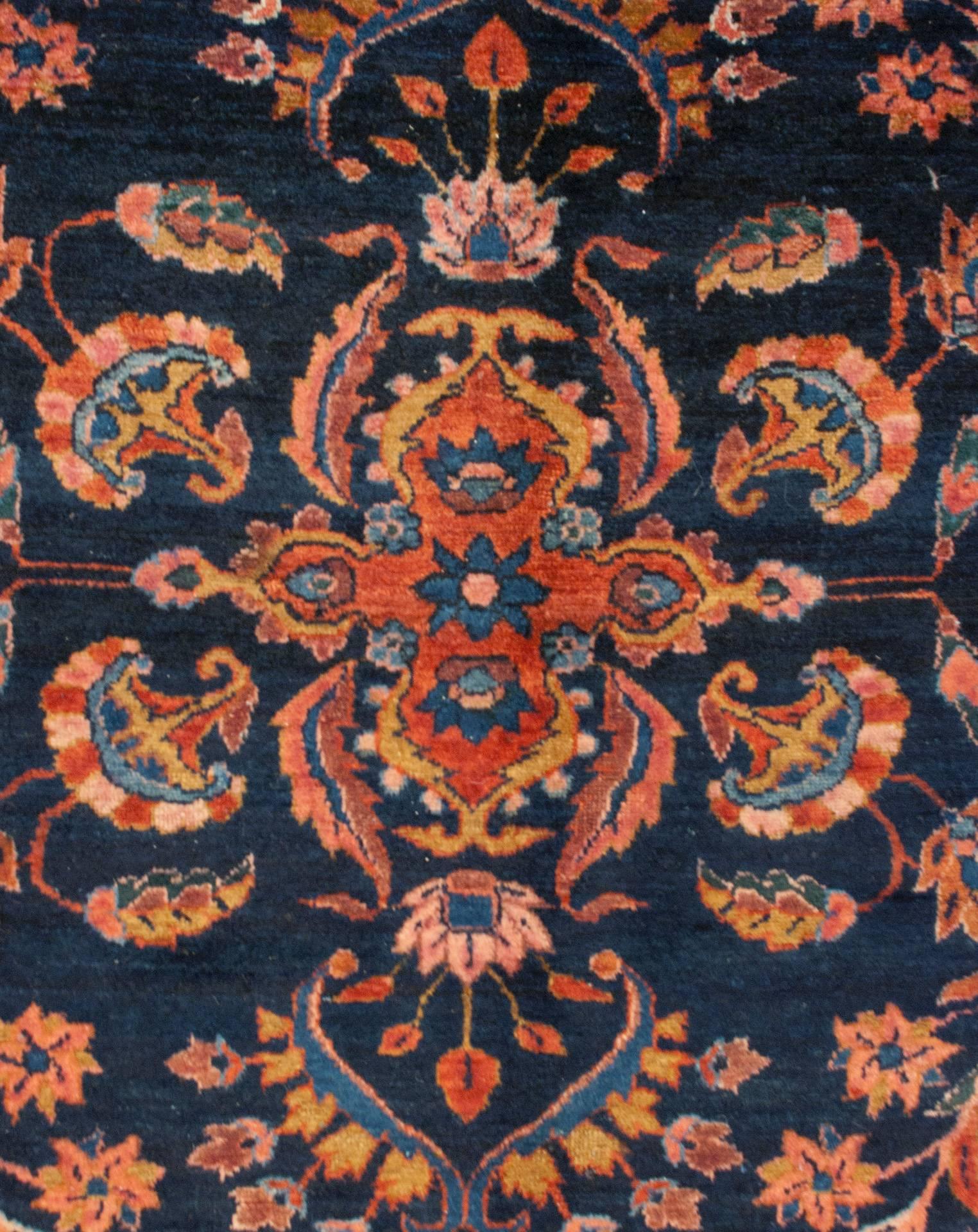 A wonderful early 20th century Persian Lilihan rug with a dark indigo background, covered by a lacy, multicolored scrolling vine and floral pattern, surrounded by a wide crimson and light indigo border with a large-scale floral pattern.