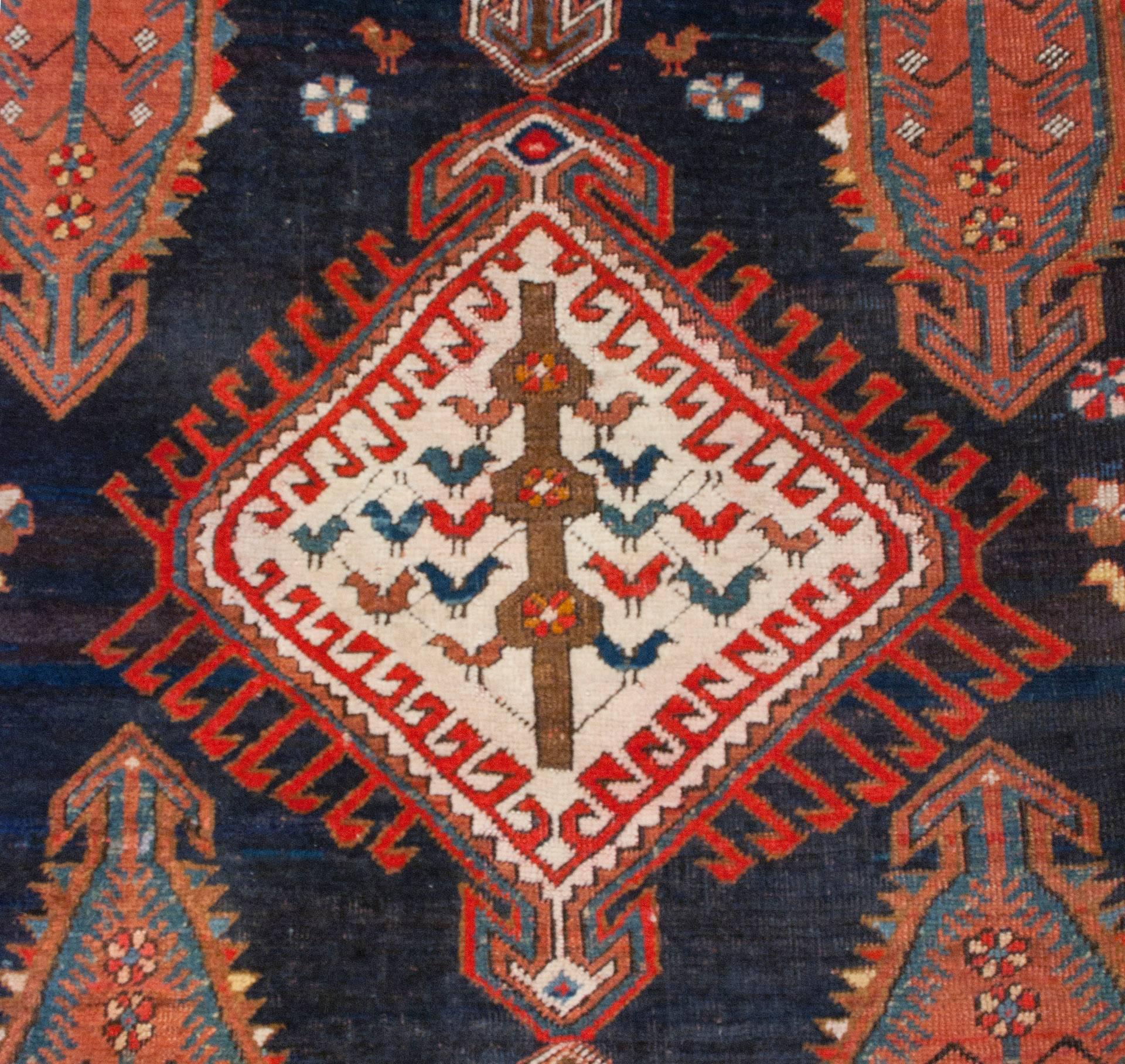 An early 20th century Persian Karabagh rug with a large central diamond medallion on an indigo background, amidst a field of large, unusual flowering tree-of-life motifs woven in crimson, natural wool, indigo and white. The rug is surrounded by a