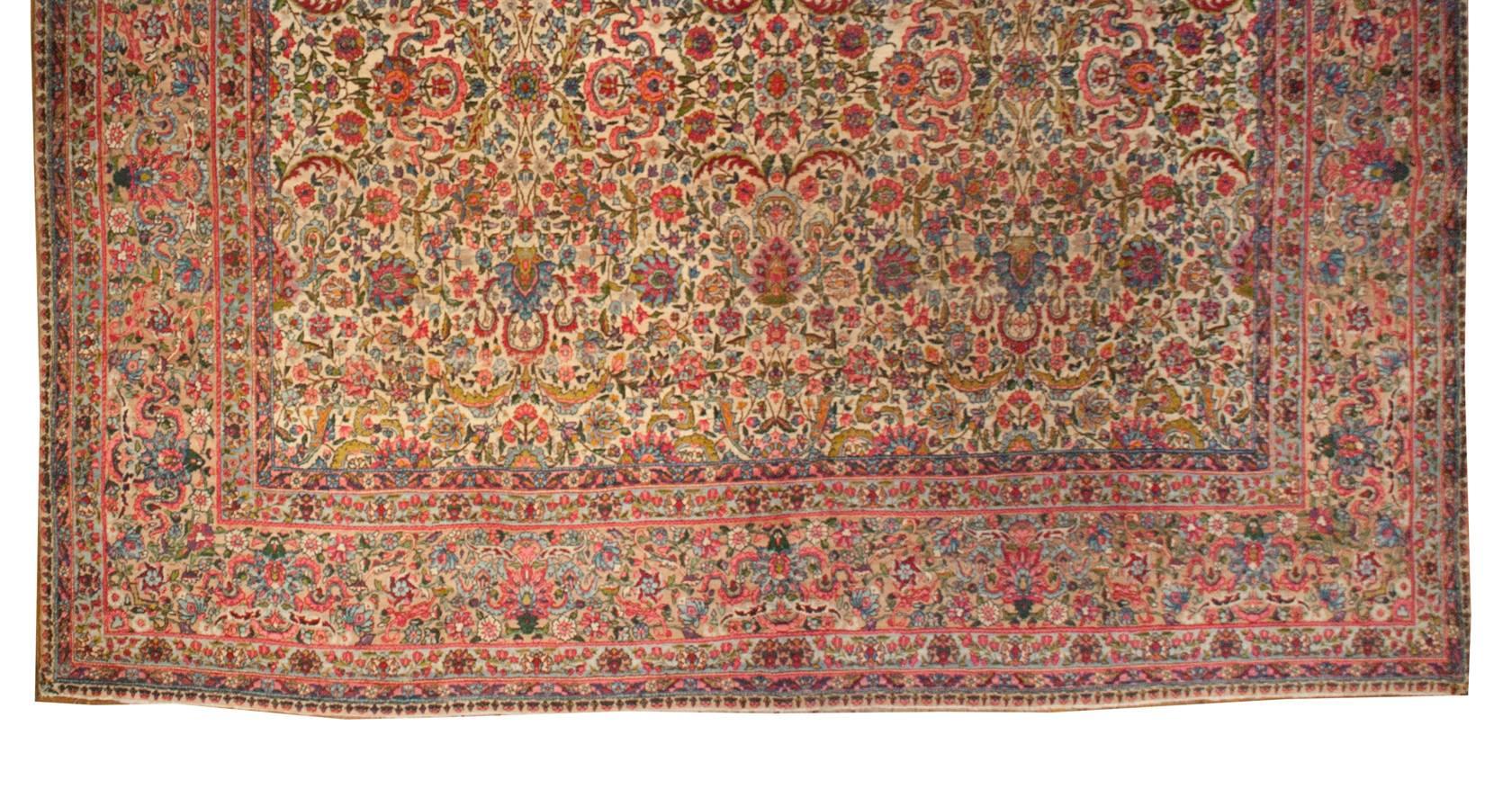 A beautiful early 20th century Persian Kirman rug with an elaborate and skillfully woven all-over multicolored pattern of interwoven large and small-scale flowers, scrolling vines and leaves, on a natural undyed background. The border is