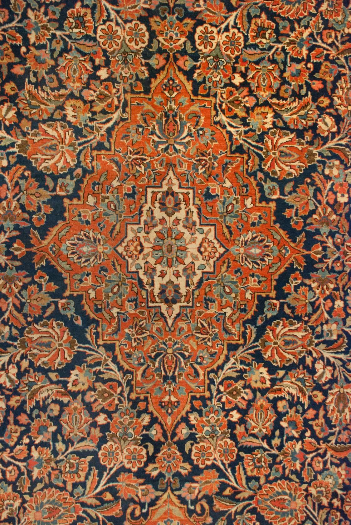 A stunning early 20th century Persian Kashan rug, woven by a highly skilled group of weavers, comprised of an all-over intensely woven light and dark indigo, crimson, cream, and mint green colored floral and scrolling vine pattern on a deep indigo