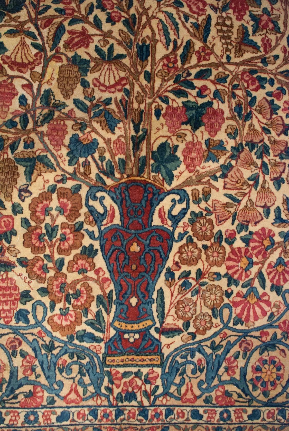 An unbelievable early 20th century Persian Kirman rug with the most amazing tree-of-life pattern sprouting from a crimson and indigo double-handled vase. The branches are heavy with myriad varieties of flowers, grapes, and petite pomegranate