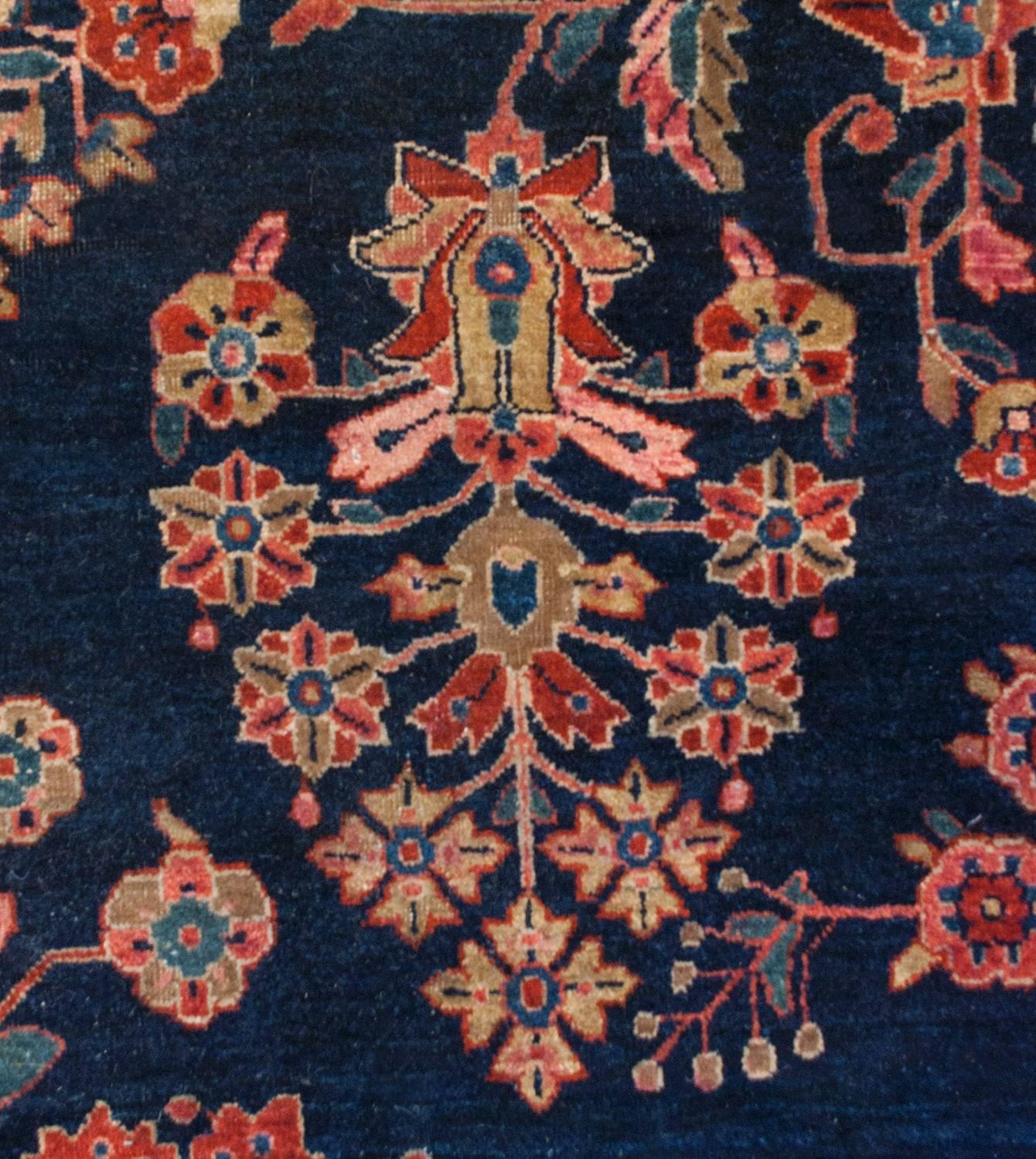 A gorgeous early 20th century Persian Sarouk rug with a wonderful large-scale floral pattern with myriad leafy and flowering branches woven in crimson, light indigo and natural, undyed, wool, all on a rich dark indigo background. The border is