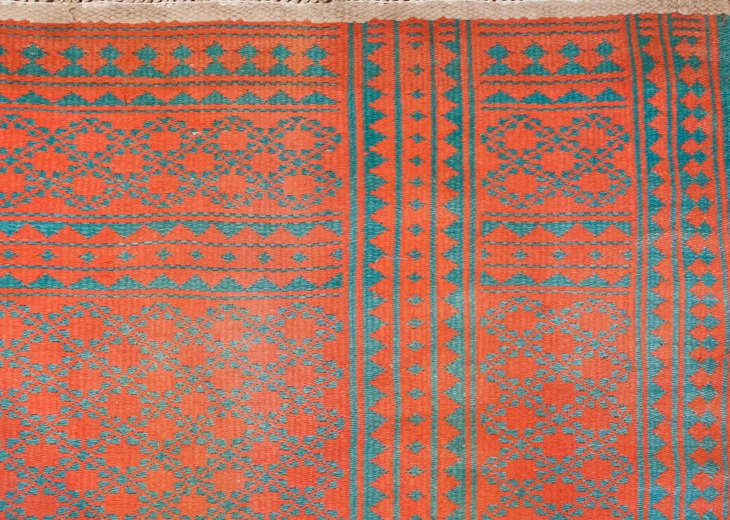 An early 20th century Persian Saveh Kilim rug, woven with naturally dyed cotton, with a beautiful all-over field of small-scale turquoise flowers on an wonderful coral background flanked by a wide border of geometric zigzag woven stripes with a