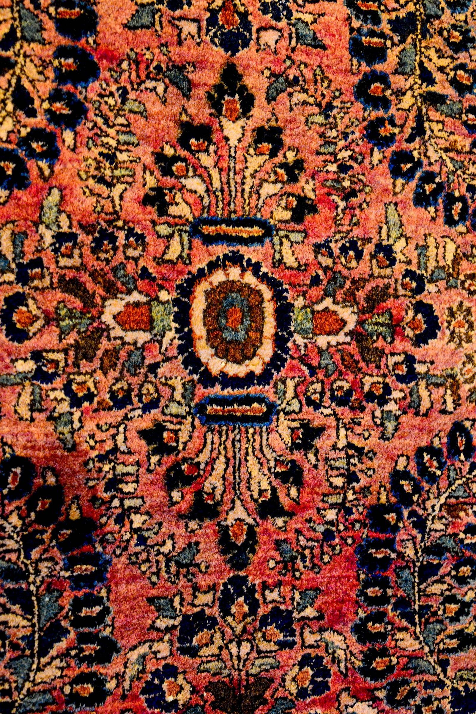 A beautifully woven early 20th century Persian Sarouk rug with a traditional all-over mirror floral pattern woven in light and dark indigo, and cream vegetable dyed wool, on a fantastic abrash cranberry background. The border is thin, with a floral