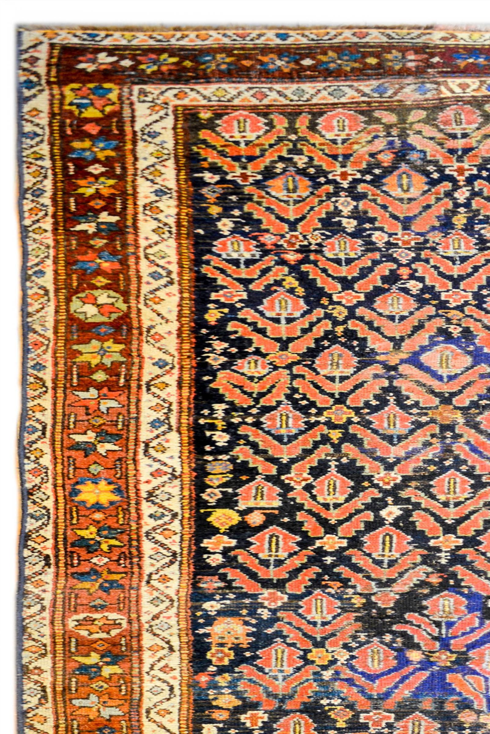 A wonderful early 20th century Kurdish runner with an all-over crimson and indigo tree-of-life pattern on a dark indigo background. The border is complex woven with a stylized floral central stripe flanked by two matching floral patterned stripes.