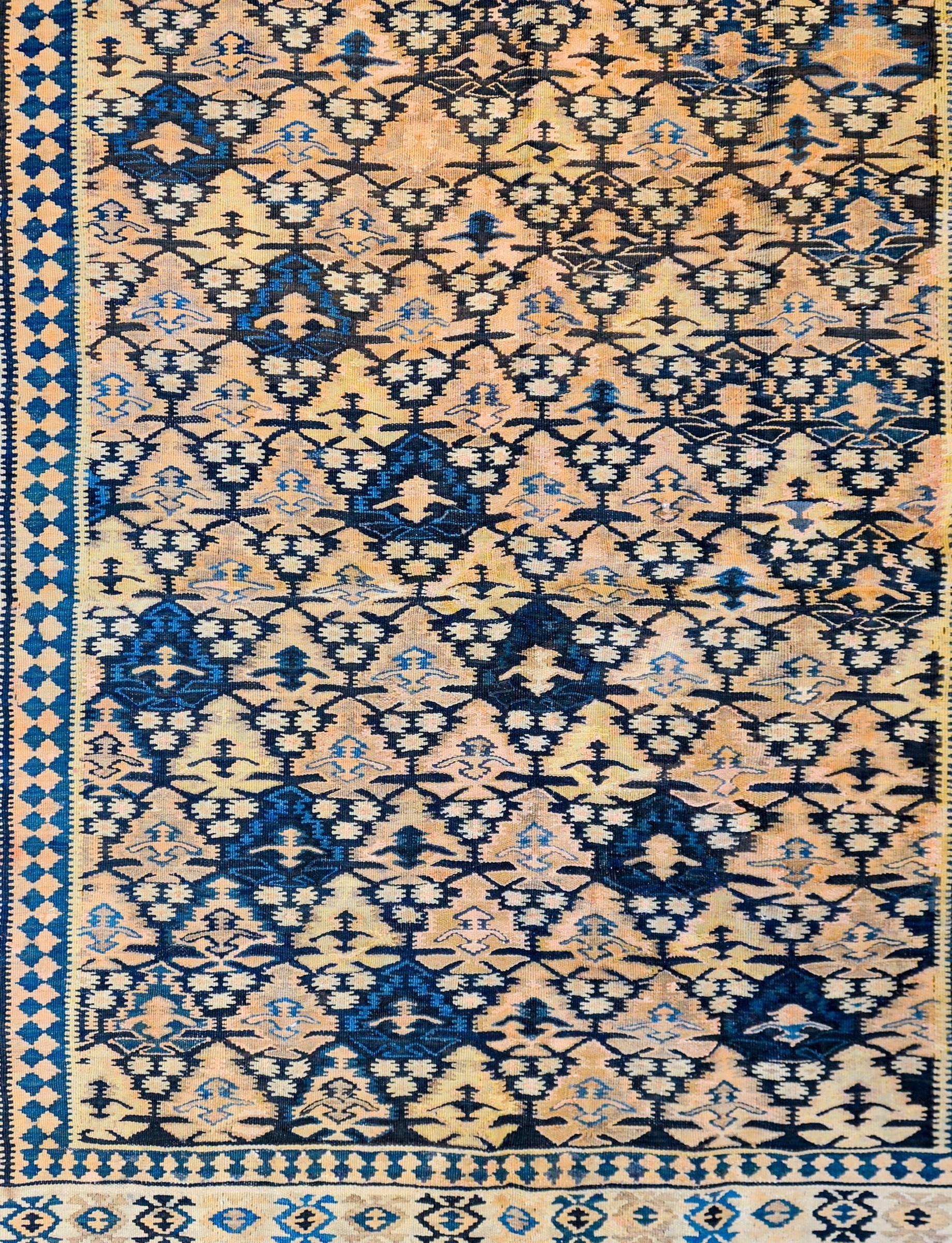 A wonderful late 19th century Persian Qazvin Kilim rug with a beautiful all-over tree-of-life pattern woven in indigo, gold, and yellow vegetable dyed wool surrounded by a complex border containing one wide central stylized floral motif flanked by