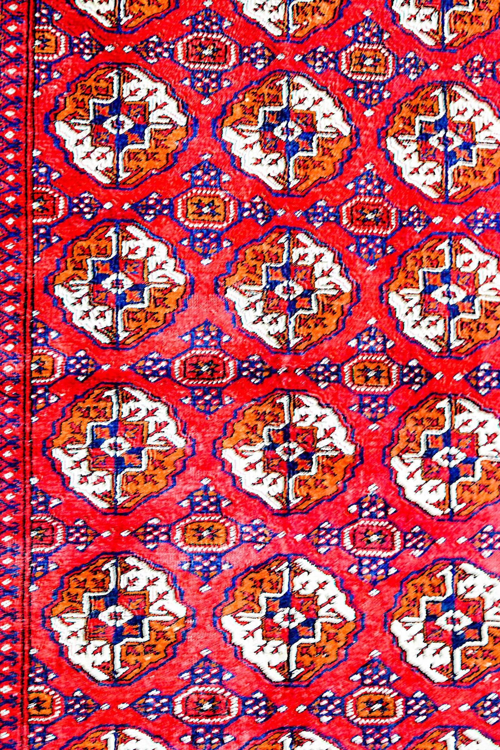 A wonderful vintage silk Turkmen rug with an all-over pattern of small medallions woven in orange, white, and indigo vegetable dyed silk on a brilliant crimson background. The border is fantastic with a wide central floral stripe flanked by multiple
