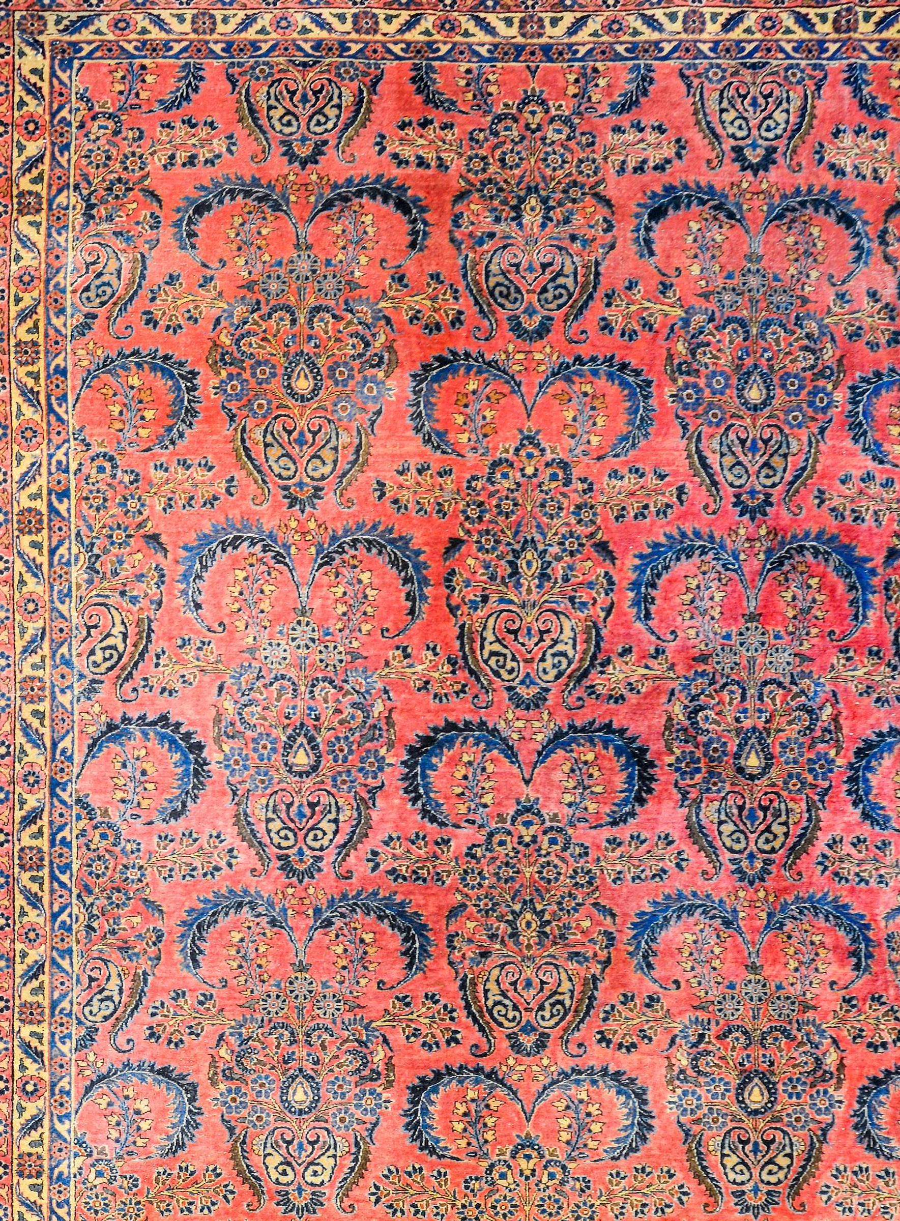 An outstanding early 20th century Persian Kashan rug with a sophisticated all-over pattern of flowering festoons woven in light and dark indigo, pink, and cream, on a beautiful coral background. The border is complementary with a wide band with