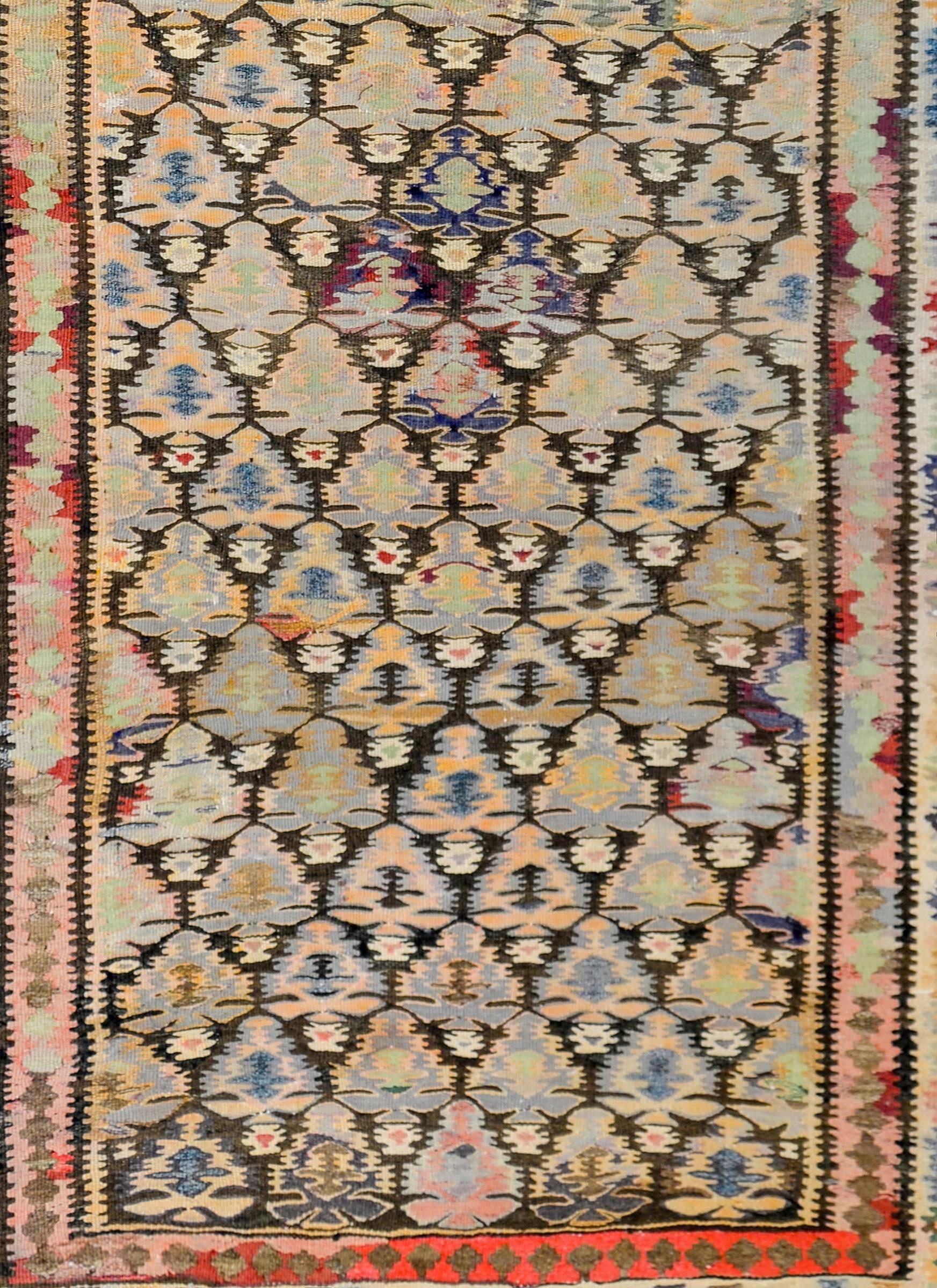 An early 20th century Persian Qazvin Kilim runner with an all-over tree-of-life pattern woven in a complex color scheme of indigo, crimson, gold, brown, and cream colored wool surrounded by a border with a stylized petite floral central stripe