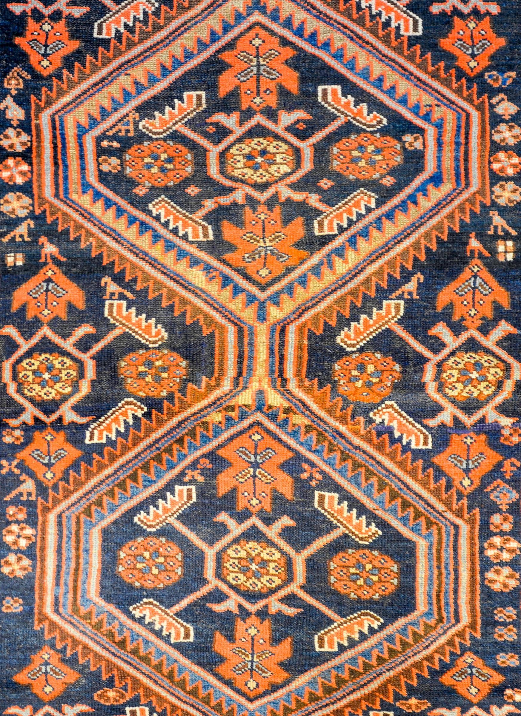 An exceptional early 20th century Kurdish rug with a fantastic pattern containing two large diamond form medallions, each with a stylized floral pattern woven in crimson, gold, and light indigo, all on a dark indigo field of stylized flowers,