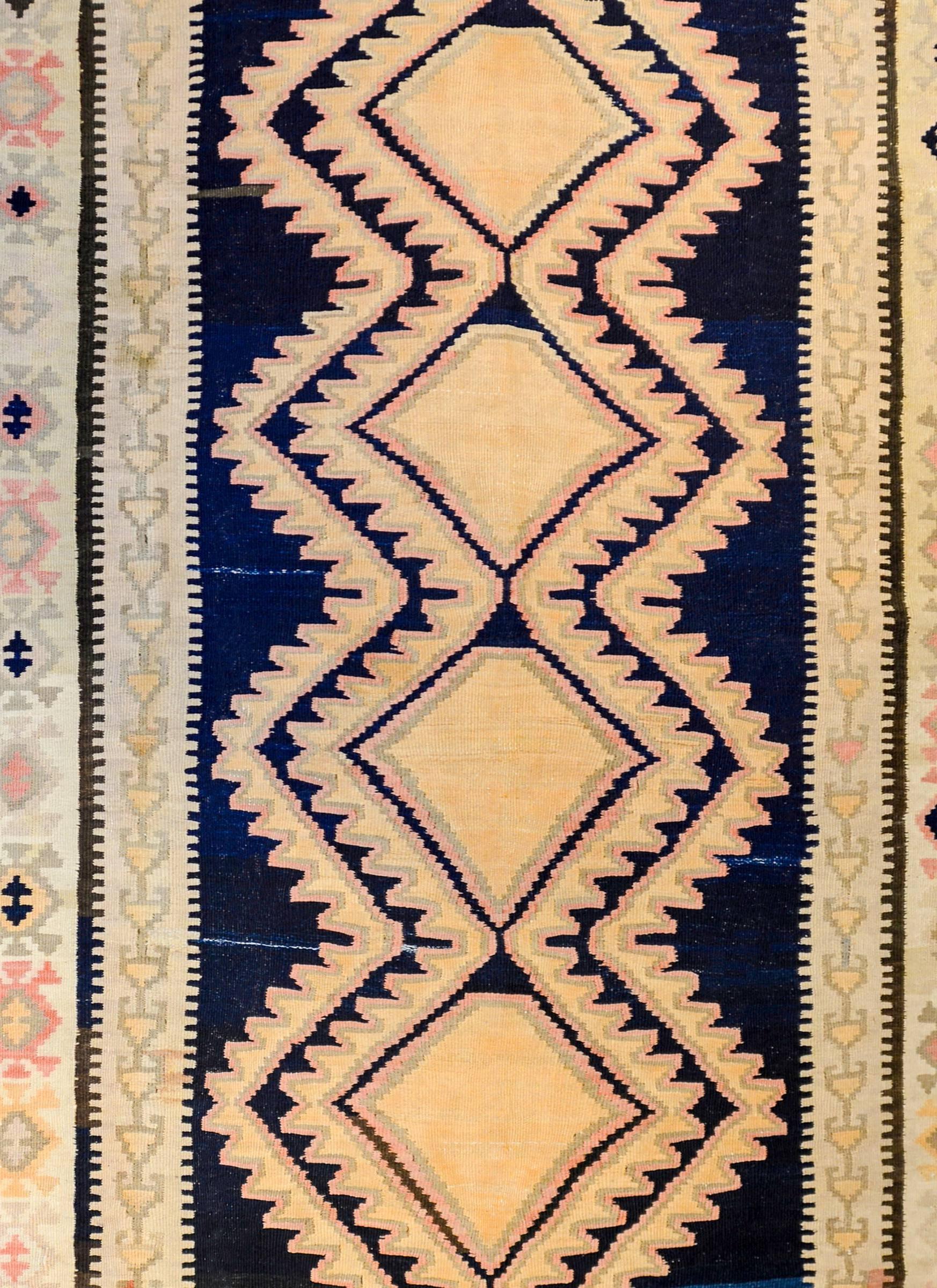 An early 20th century Persian Ersin wide Kilim runner with an incredible pattern woven with six large gold diamond medallions flanked with two gold and pale pink zigzag stripes on a dark abrash indigo background. The border is composed with two