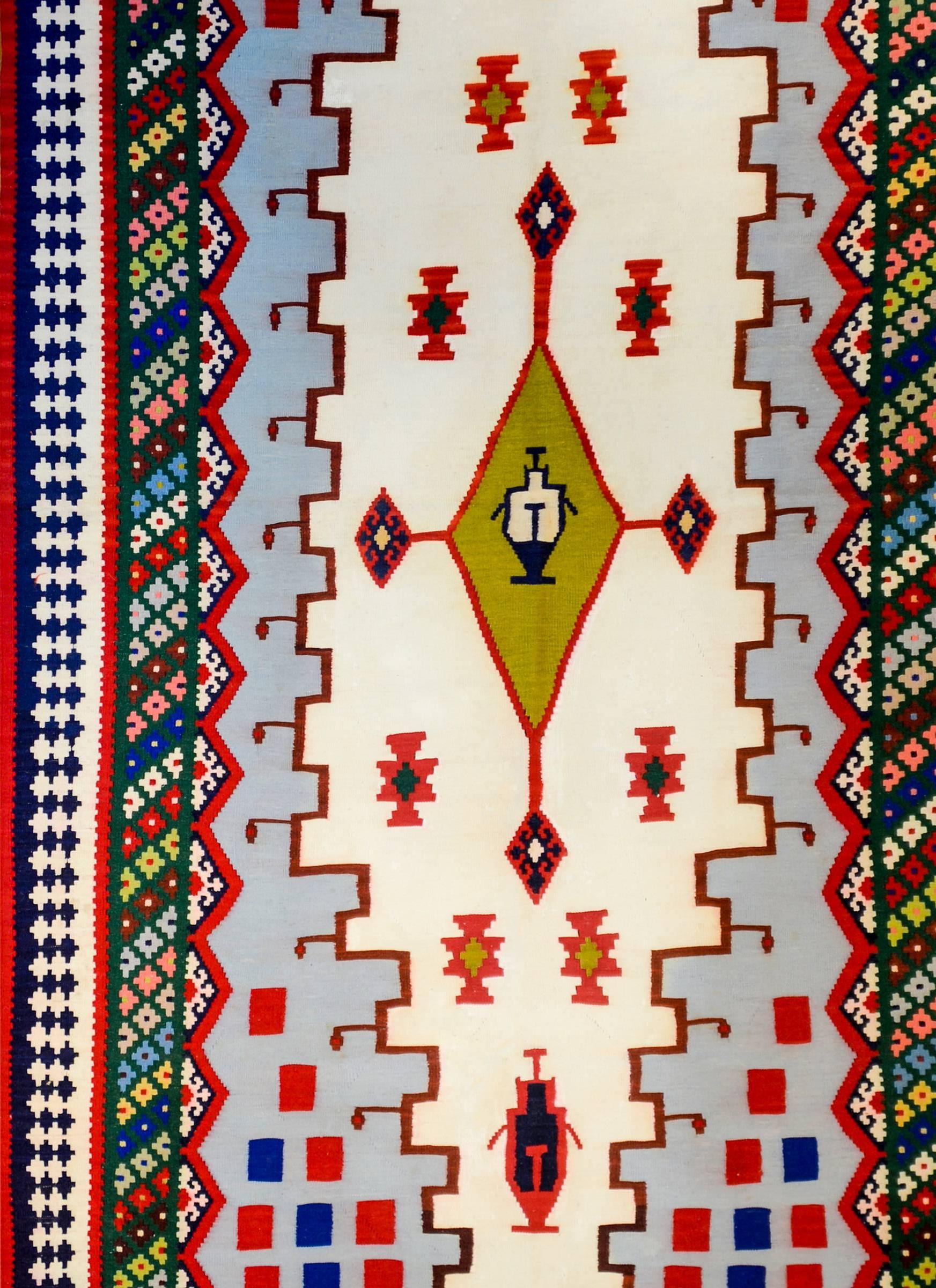 A beautiful early 20th century Persian Shiraz Kilim rug with a fantastic central chartreuse diamond medallion midst a field of stylized flowers on a cream colored background. The border is complex with multiple multicolored geometric patterned