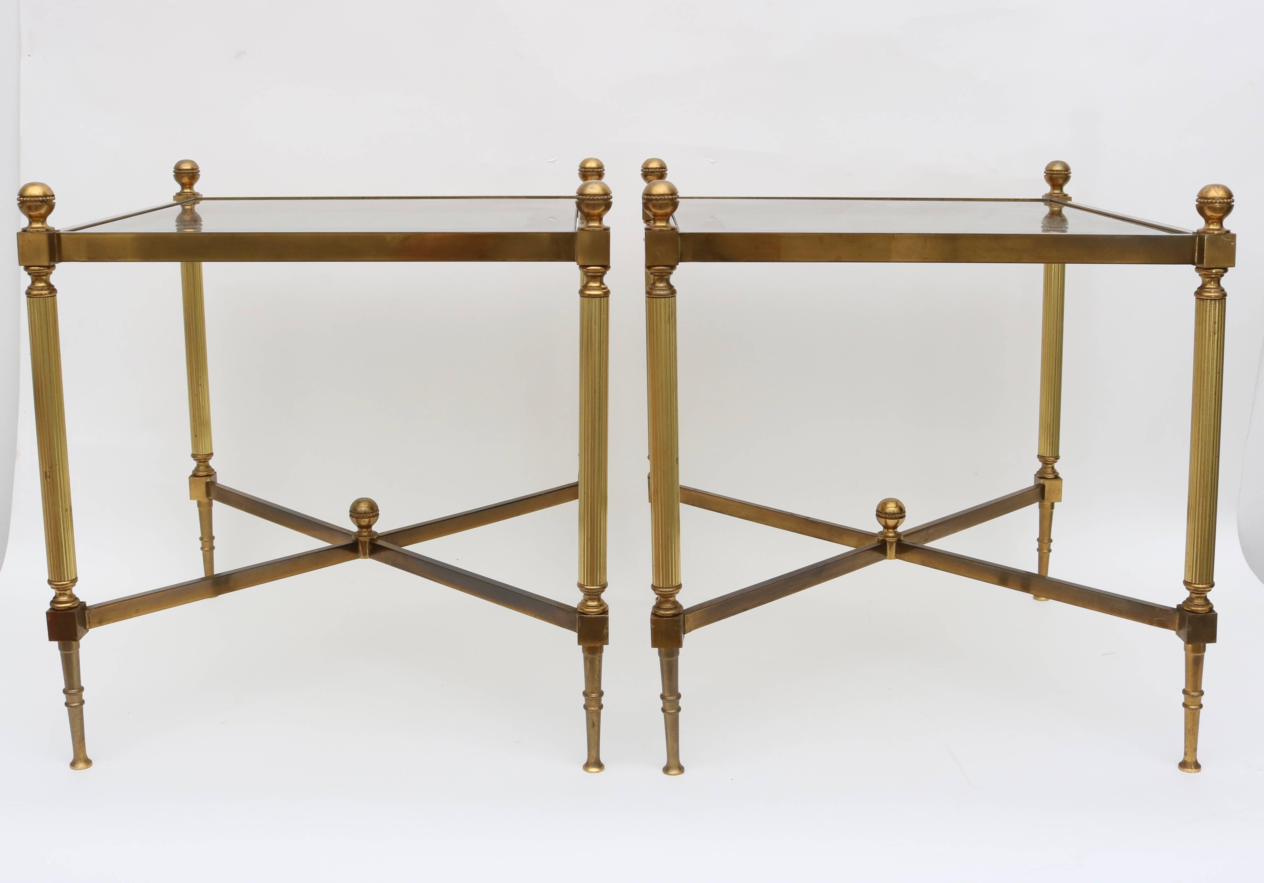 This stylish pair of Maison Jansen style tables date to the 1960s and are fabricated in brass with an X-form cross stretcher and fluted legs. The inset glass tops have a antiqued-gold painted border on the underside.

Note: Height to top of finial