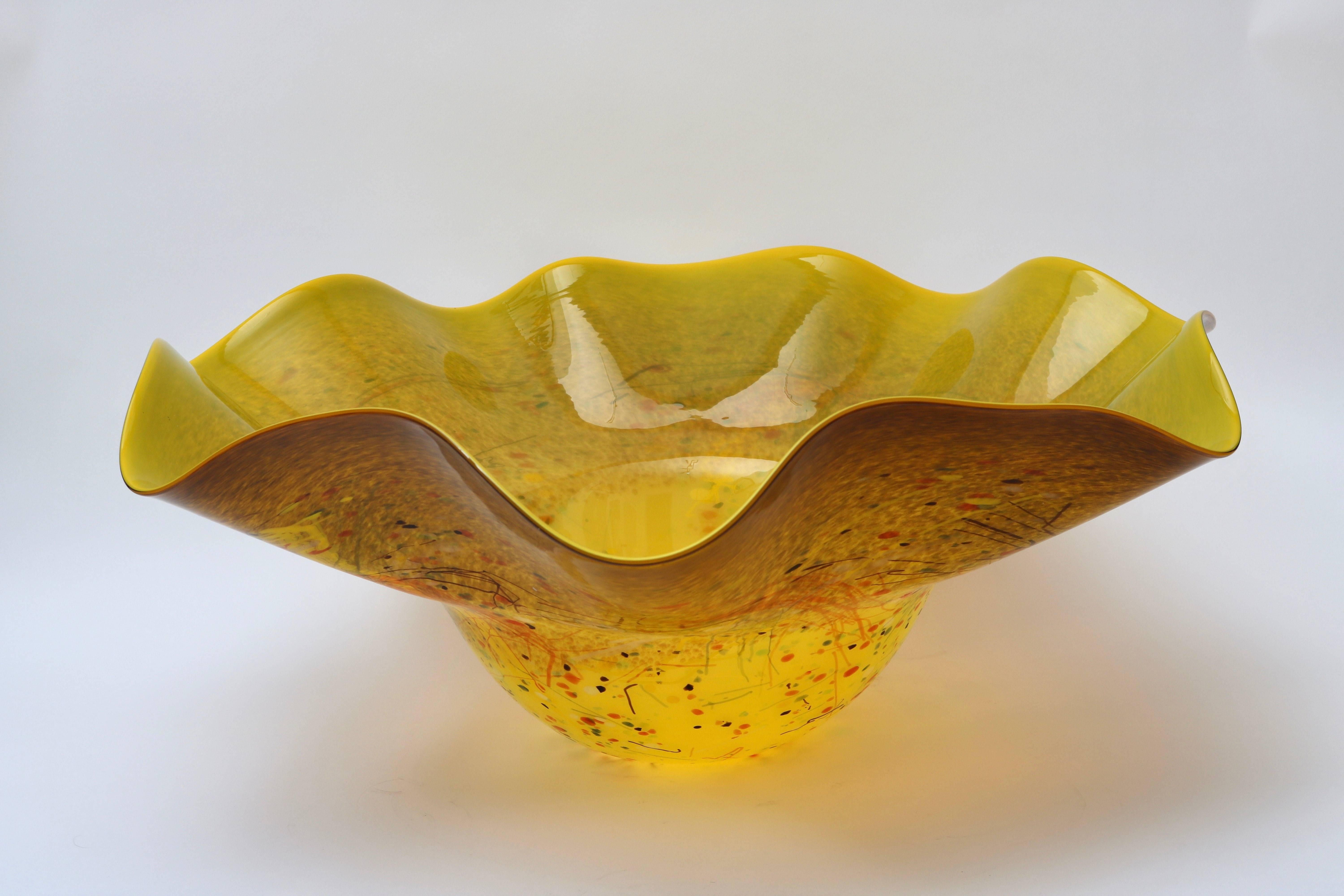 This stylish art glass bowl is very much in the style of pieces created by Dale Chihuly and was recently purchased from a Palm Beach estate. The free-form has stylized floral form and has a golden marigold coloration with flecs of color