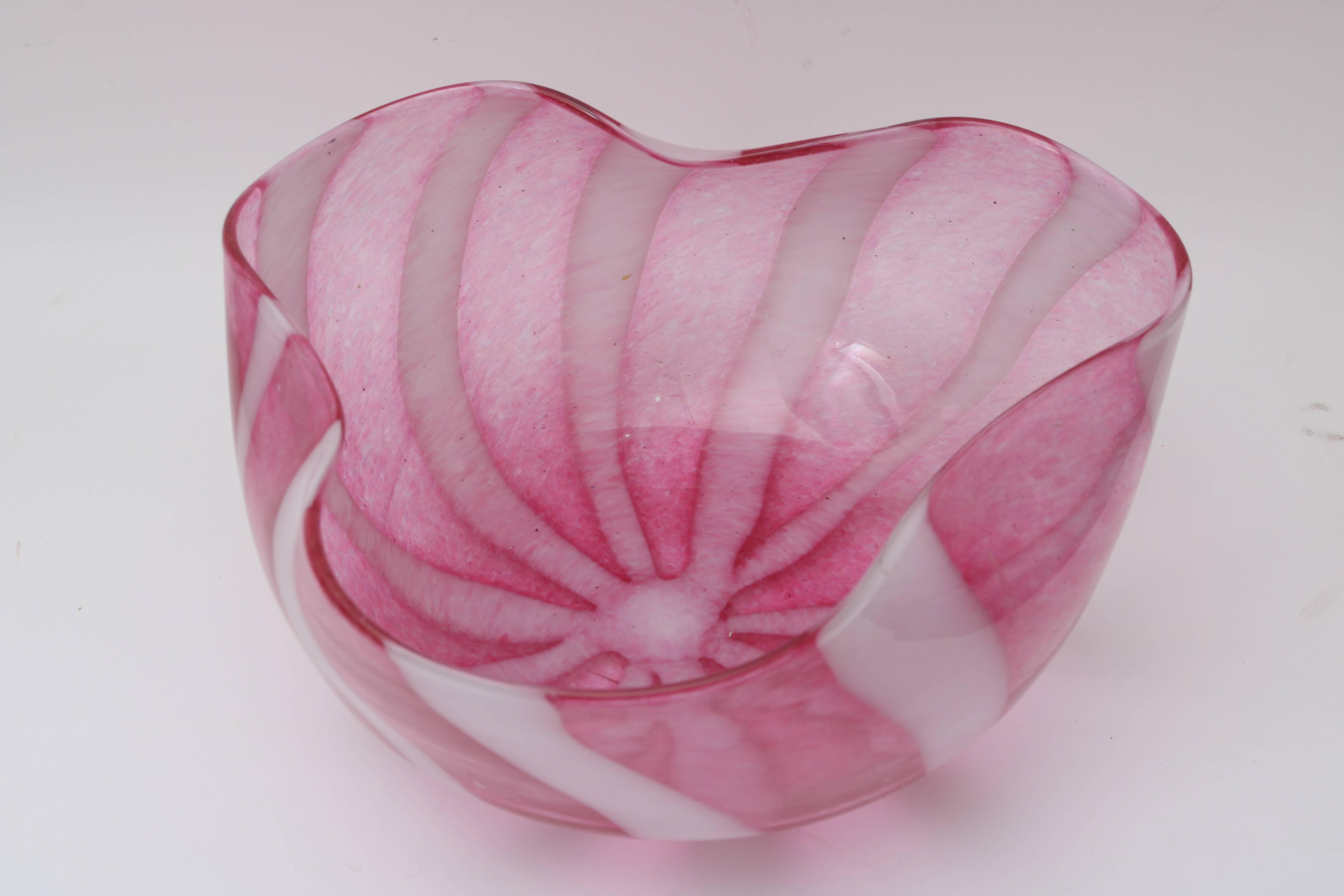This stylish Murano glass bowl dates from the Mid-Century and seems to capture an open flower bloom with its free-formed rim. The colors are a translucent raspberry and white in a ribbon motif.

For best net trade price or additional questions