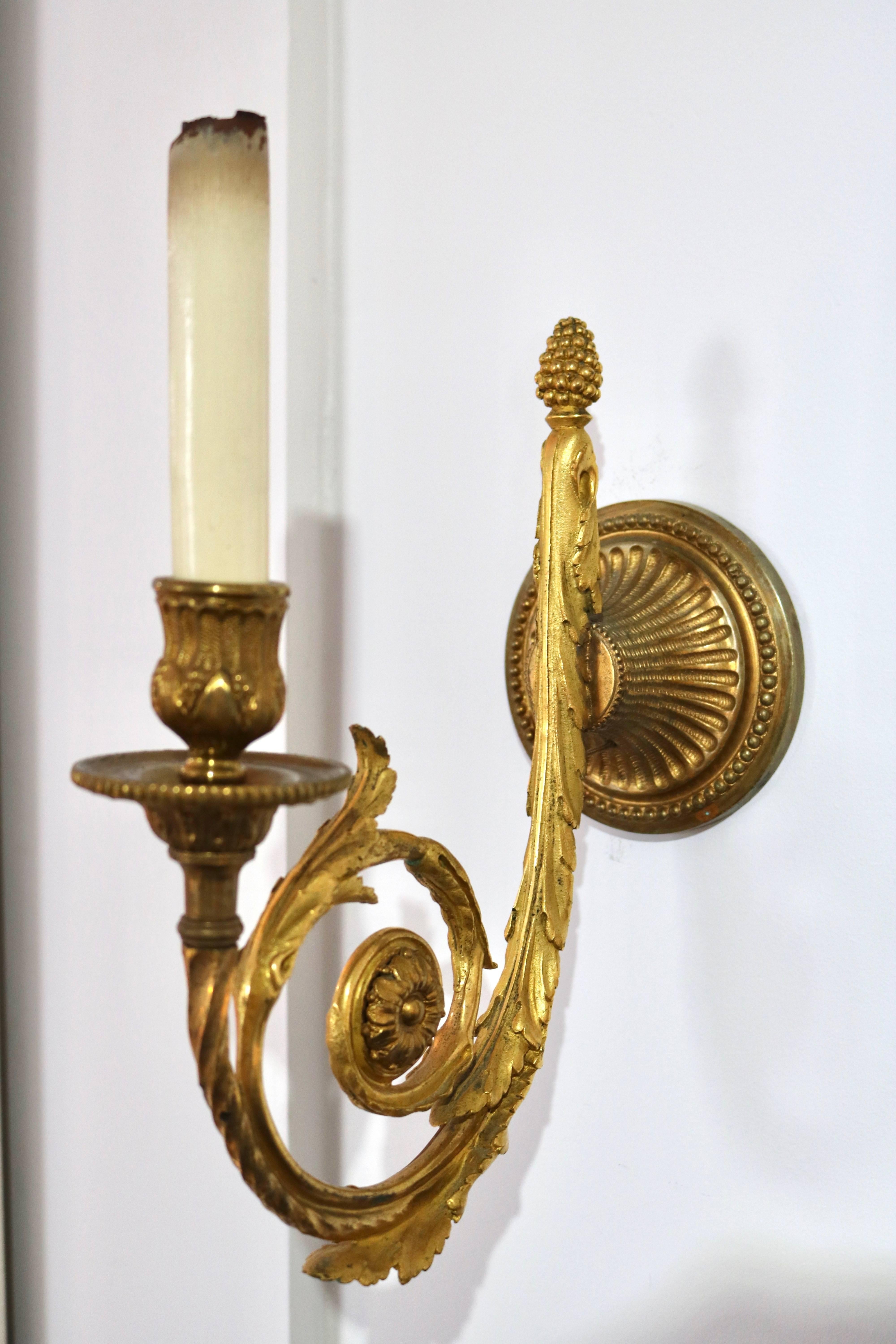 This stylish pair of wall sconces are in the Louis XVI taste and date from the late 19th century. The bronze doré is a combination of gilt gold and an antique gold coloration. They retain their original wood candle sleeves in an antique white