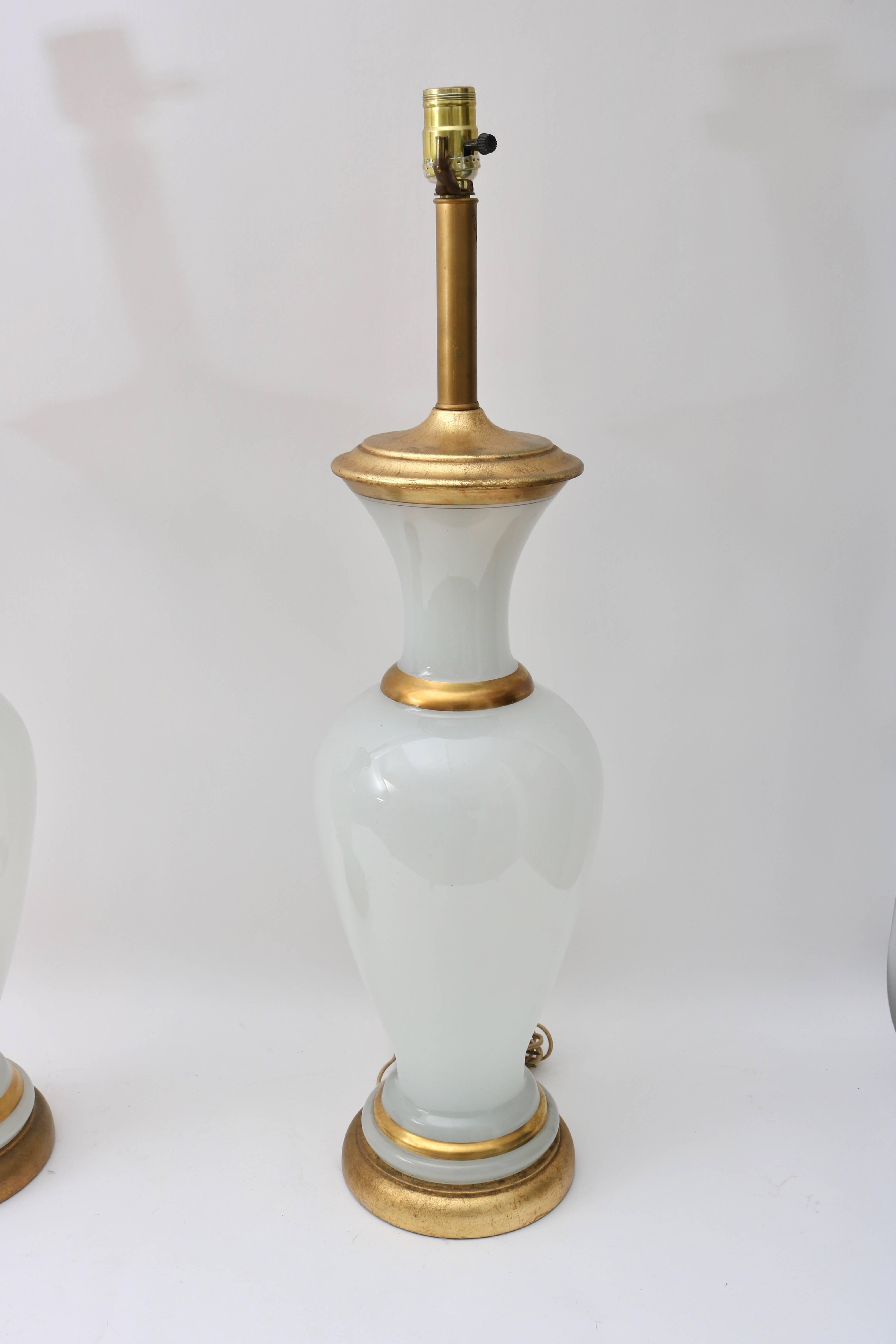Cette paire de lampes de table élégante est tout à fait dans le style des années 1960 avec sa couleur et sa forme sophistiquée Hollywood Regency. Le verre opalin est rehaussé de bandes dorées et d'une base et d'un capuchon en feuilles