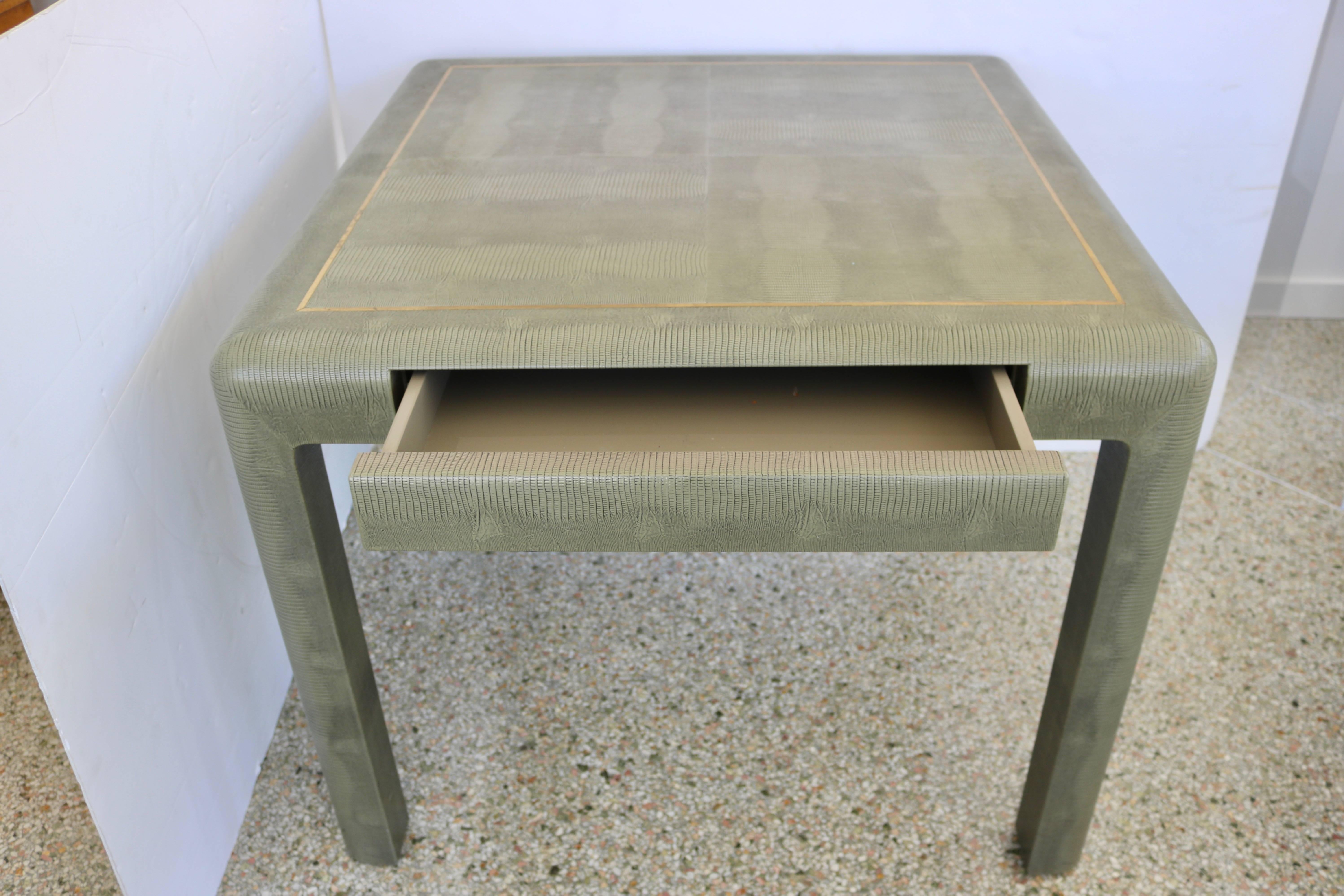 This stylish game table was created by Karl Springer and dates to the 1986. It is fabricated with a faux lizard vinyl fabric, detailed with an inset brass trim. And a single drawer that can be used for storage purposes.

Note: Image # 10 for Karl