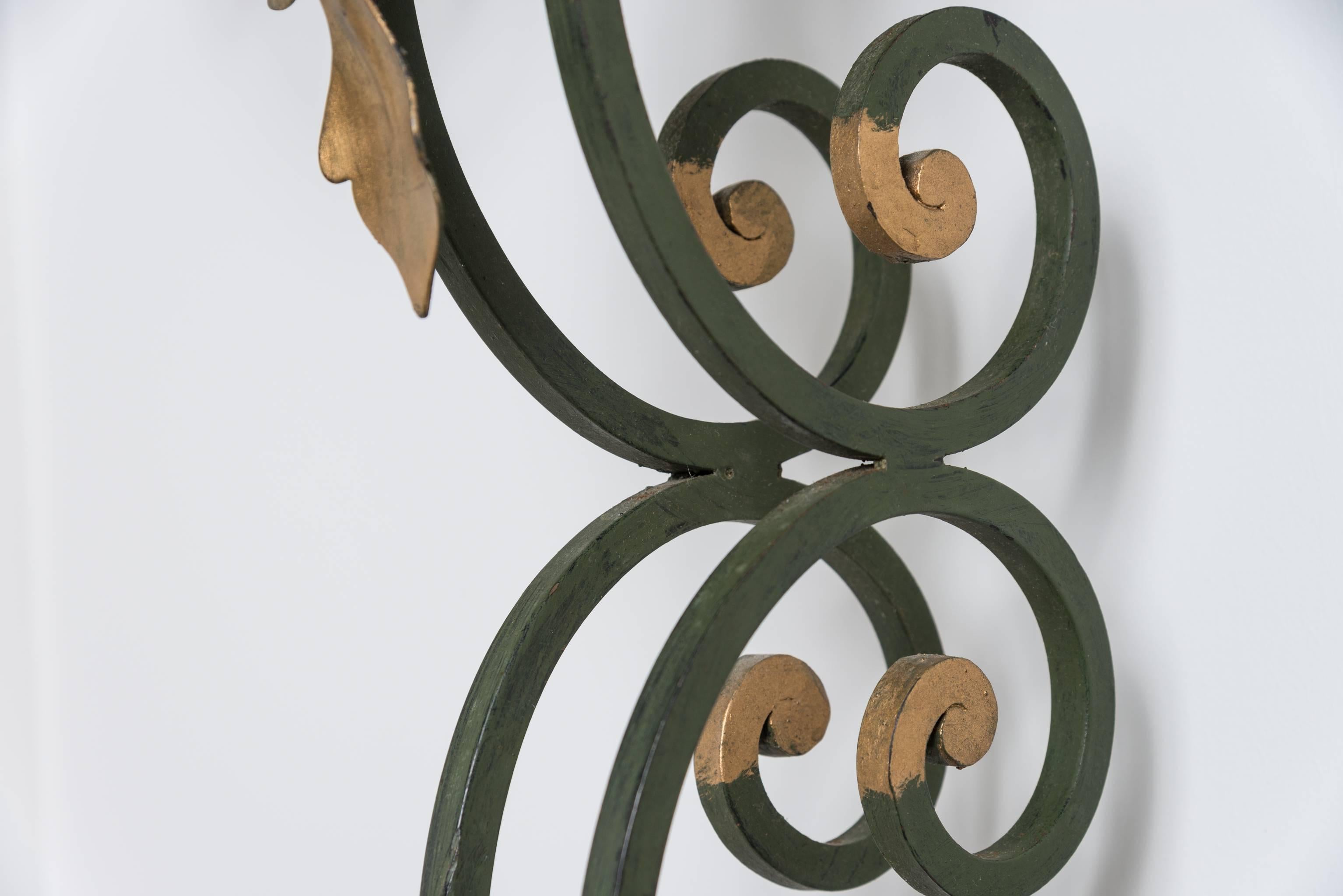 This set of Louis XV style wall hung demilune consoles date from the 1920s-1930s and were purchased in France. The stylized half of a cupids-bow central support and apron are wrought iron with a Verdi green painted finish and the acanthus leaves are