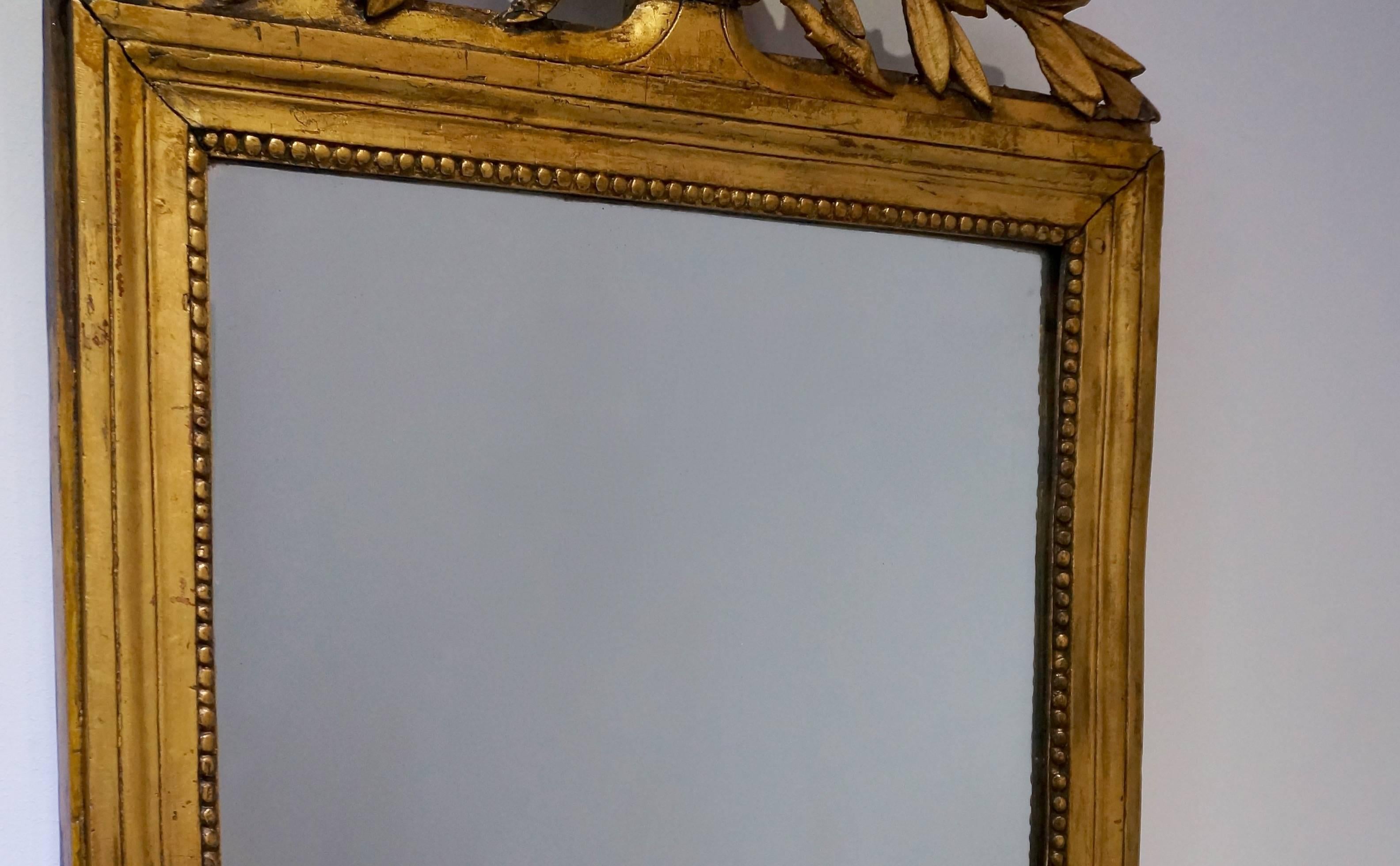 This mirror was created in France in the early part of the 19th century circa 1820, during the French-Regency period. With its Classic lines very reminiscent of the Louis XVI period and crowned with two berry-laden fronds, sheet music and a