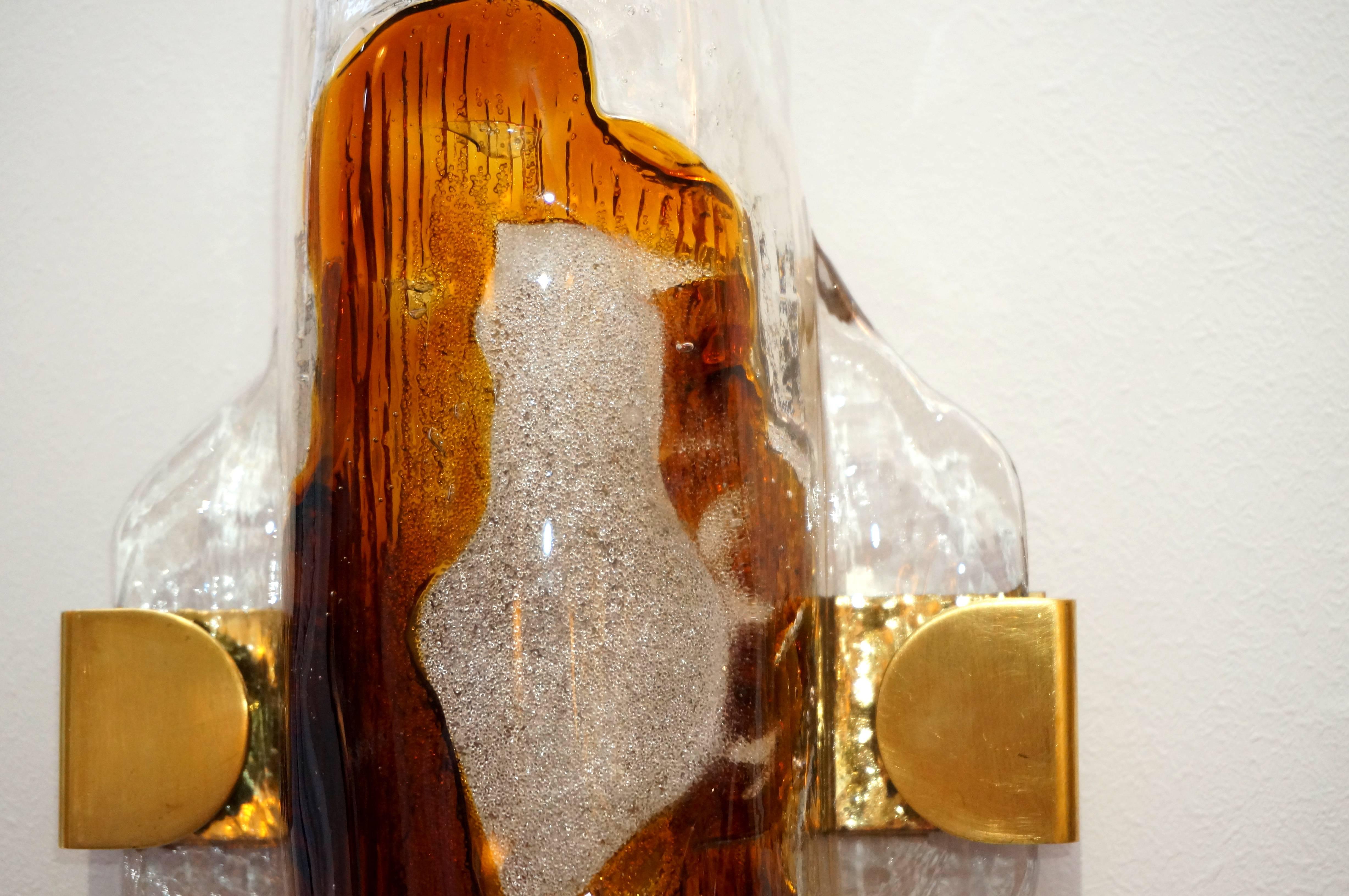 This pair of Mid-Century Modern wall sconces were created in the 1960s by the iconic Mazzega of Italy.

They are in Murano glass in an organic, molten form of clear and amber coloration. The hardware is a polished brass and they require one
